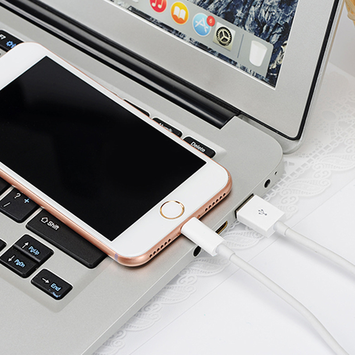 Ein weißes Smartphone ist über ein weißes Ladekabel mit einem Laptop verbunden. Der Laptop ist auf einem Tisch geöffnet.