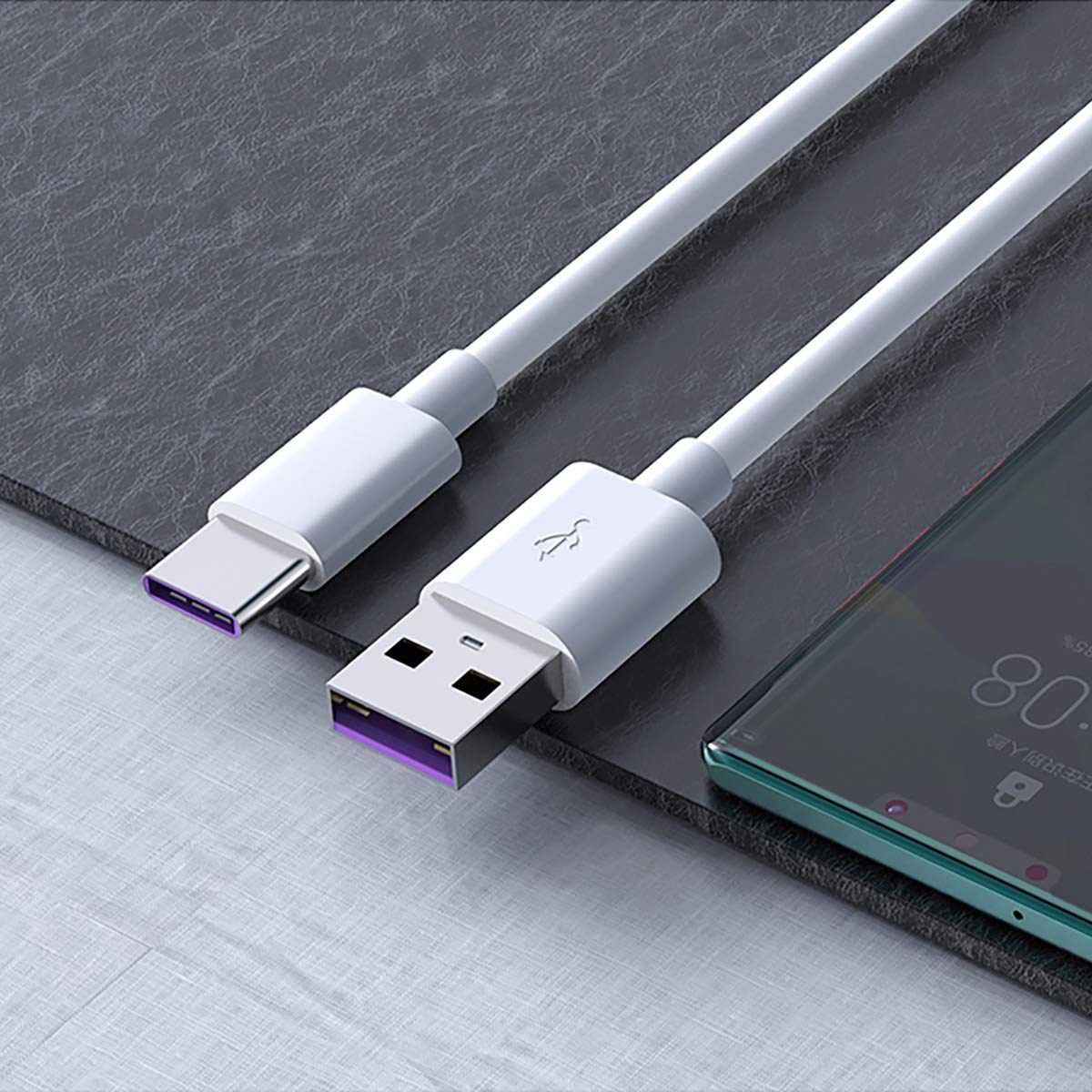Ein weißes USB-Ladekabel liegt auf einer dunklen Oberfläche, in der Nähe eines Telefons, das die Uhrzeit anzeigt. Das Kabel hat lila Akzente.