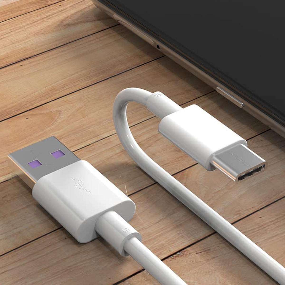 Ein weißes USB-C-Ladekabel mit USB-A-Anschluss liegt auf einer Holzoberfläche neben einem Smartphone.