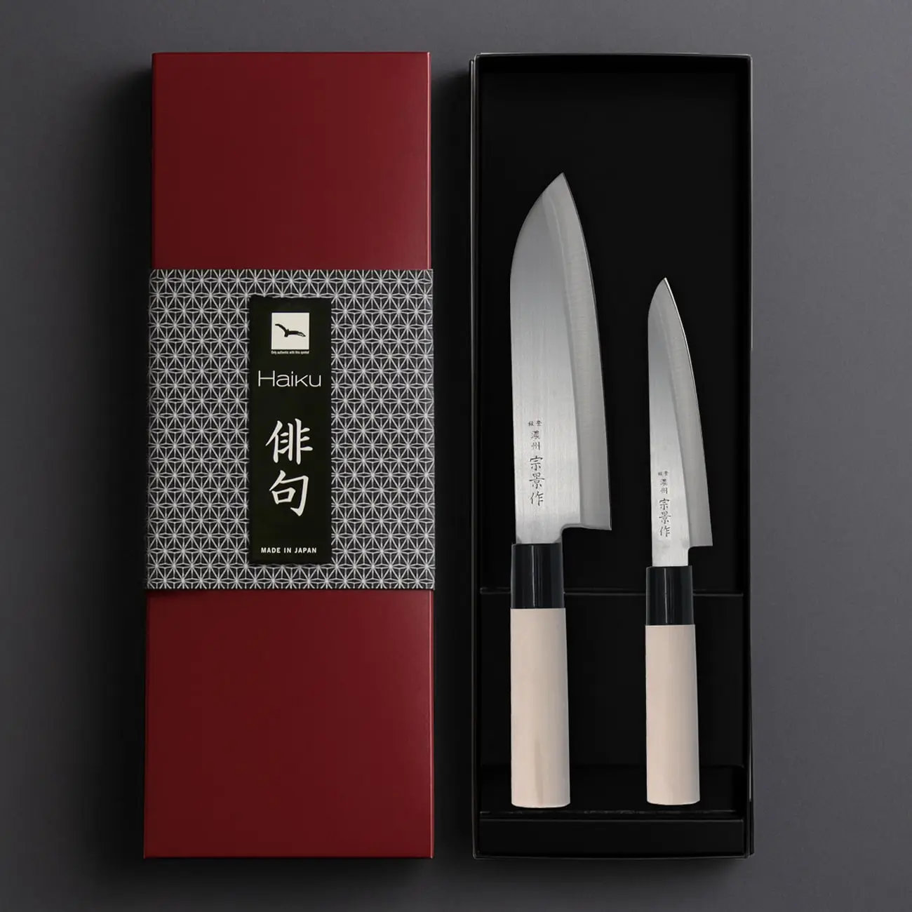 Zwei japanische Messer in einer schwarzen Box, neben einer roten Box mit Haiku-Branding. Messer haben weiße Griffe.