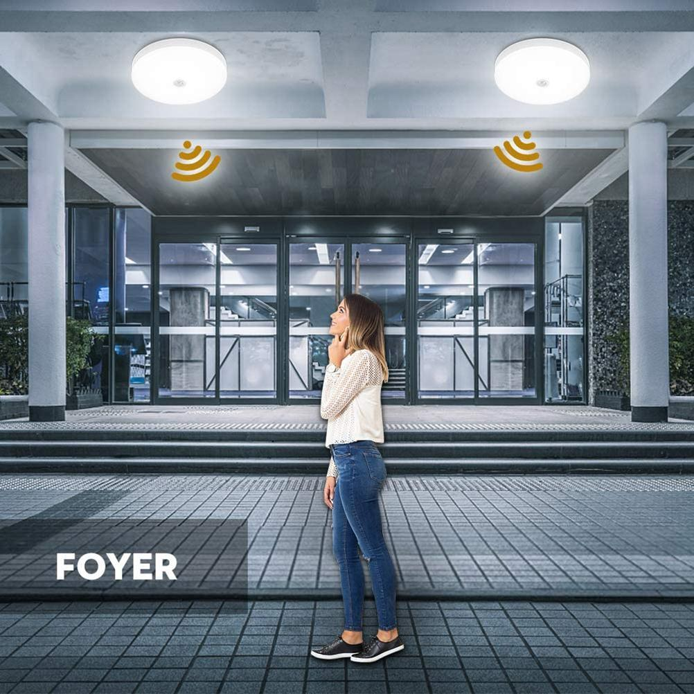 Eine Frau steht in einem Foyer und blickt nach oben. Zwei Lichter mit Sensoriksymbolen sind darüber. Glastüren und Stufen sind im Hintergrund.