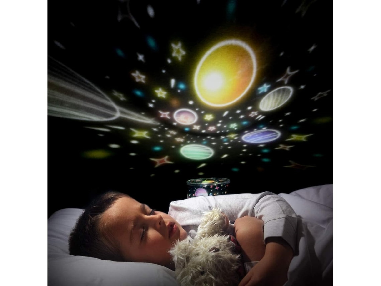 Ein Kind schläft mit einem Teddybären unter einem projizierten Sternenhimmel. Planeten und Sterne sind vor schwarzem Hintergrund sichtbar.