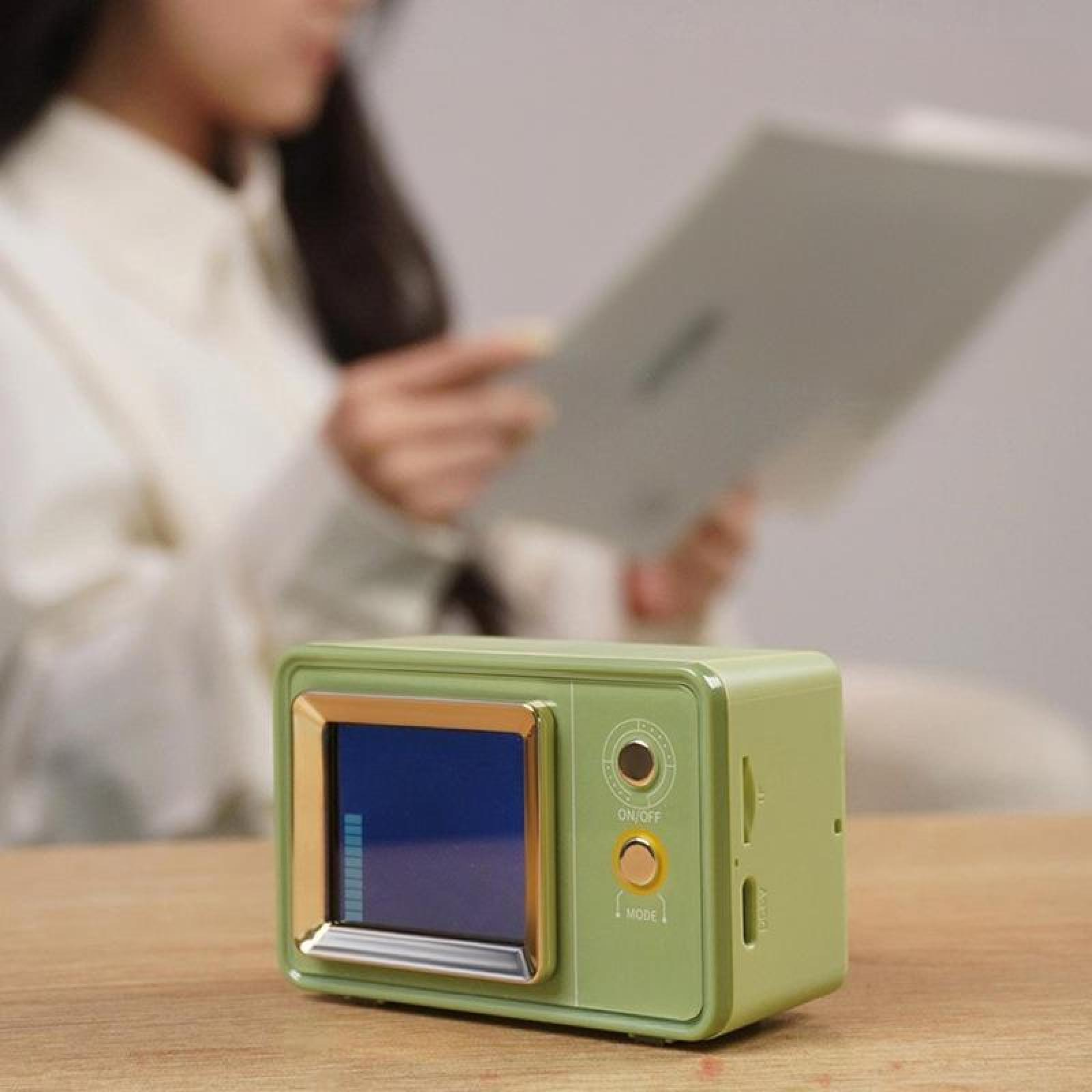 Grünes Retro-Radio mit Bildschirm steht auf einem Tisch. Im Hintergrund liest eine Person ein Buch.