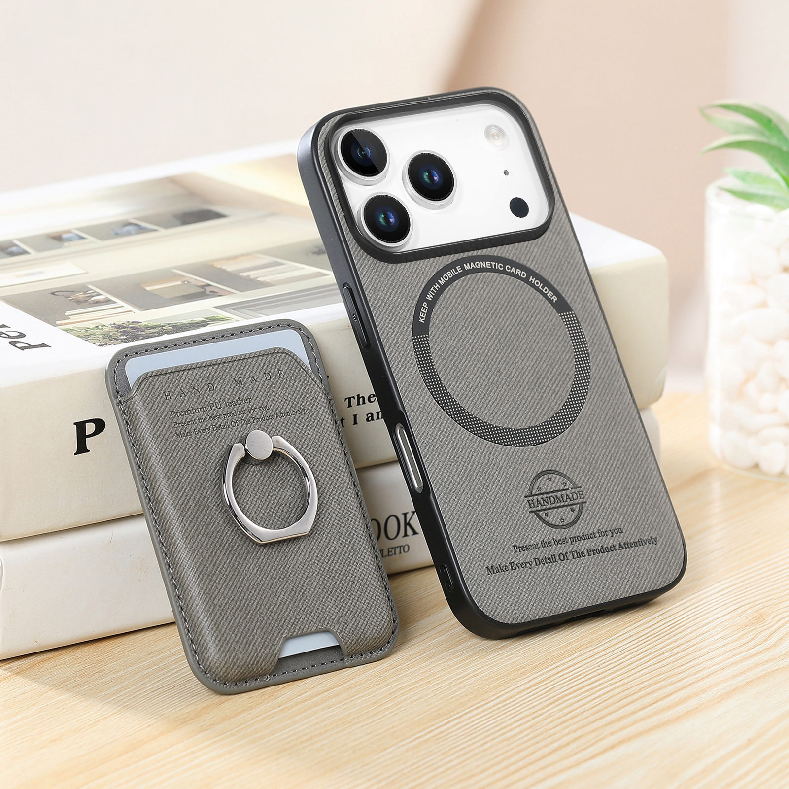 Una custodia per telefono e un porta carte, entrambi grigi, poggiano su libri. La custodia ha lenti della fotocamera. Il supporto ha un anello.
