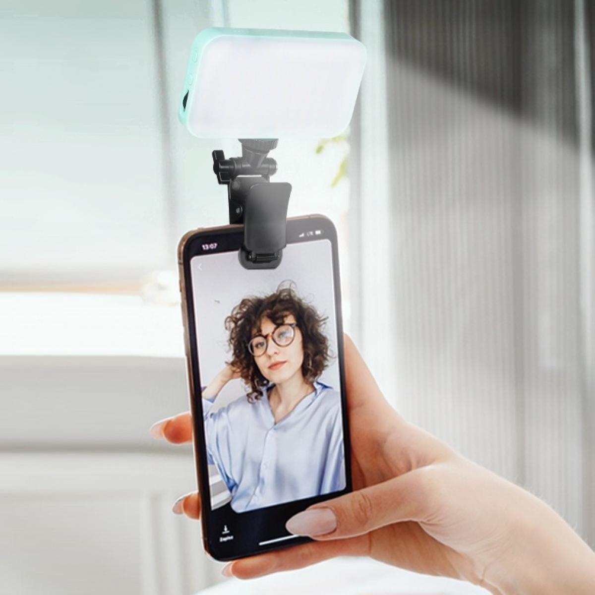Ein Telefon zeigt ein Selfie einer Frau, gehalten von einer Hand. Oben ist ein Licht angebracht.