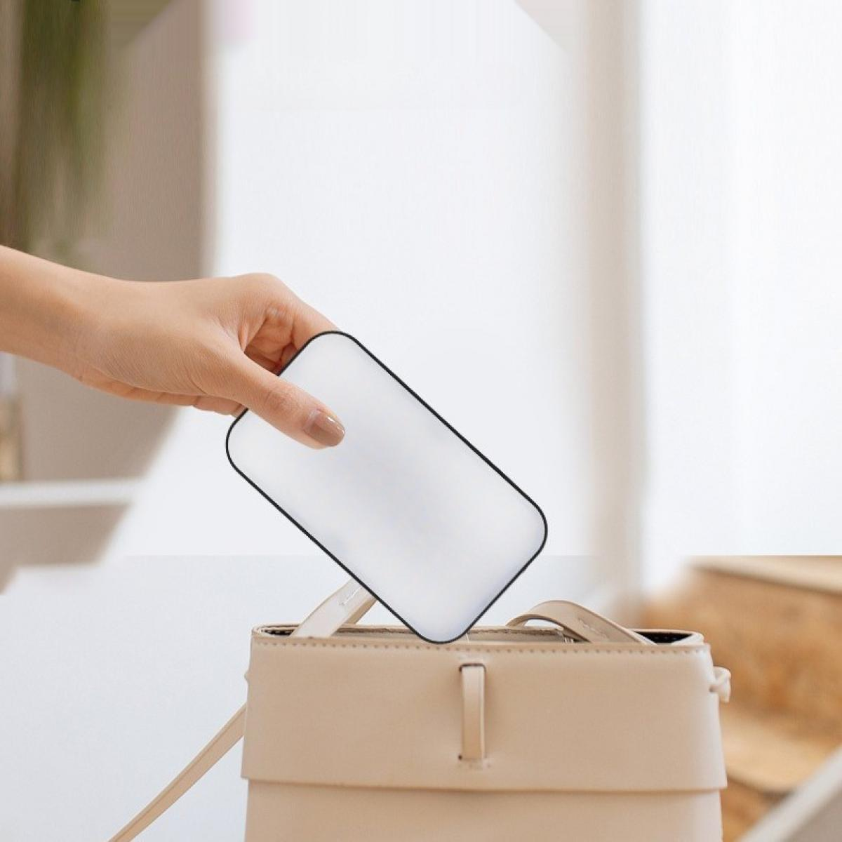 Eine Hand legt ein weißes Gerät mit schwarzem Umriss in eine beige Handtasche. Der Hintergrund ist ein verschwommenes Interieur.