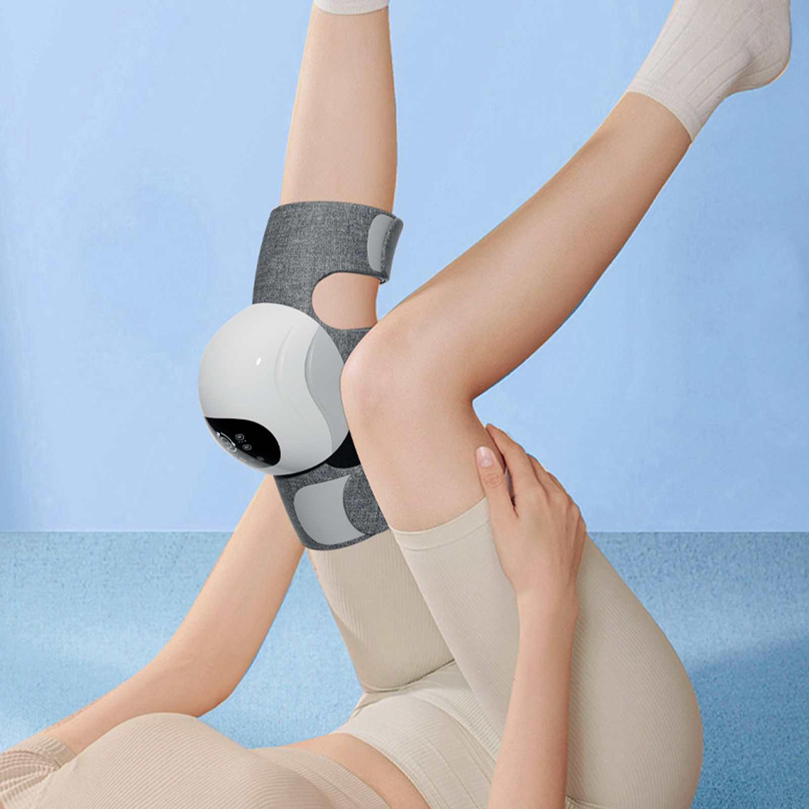 Person mit Knieorthese auf dem Bein, liegend. Weißes Gerät am Knie, graue Orthese, beige Kleidung, hellblauer Hintergrund.