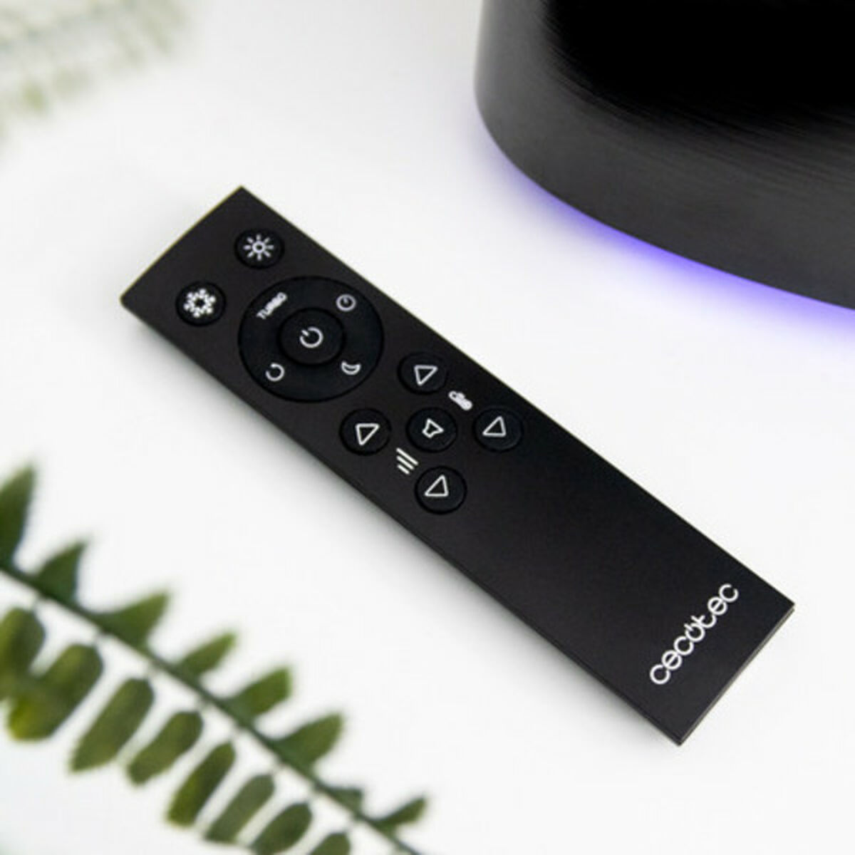 Un telecomando nero con vari pulsanti, tra cui accensione/spegnimento, direzionali e di funzione, è su una superficie bianca.