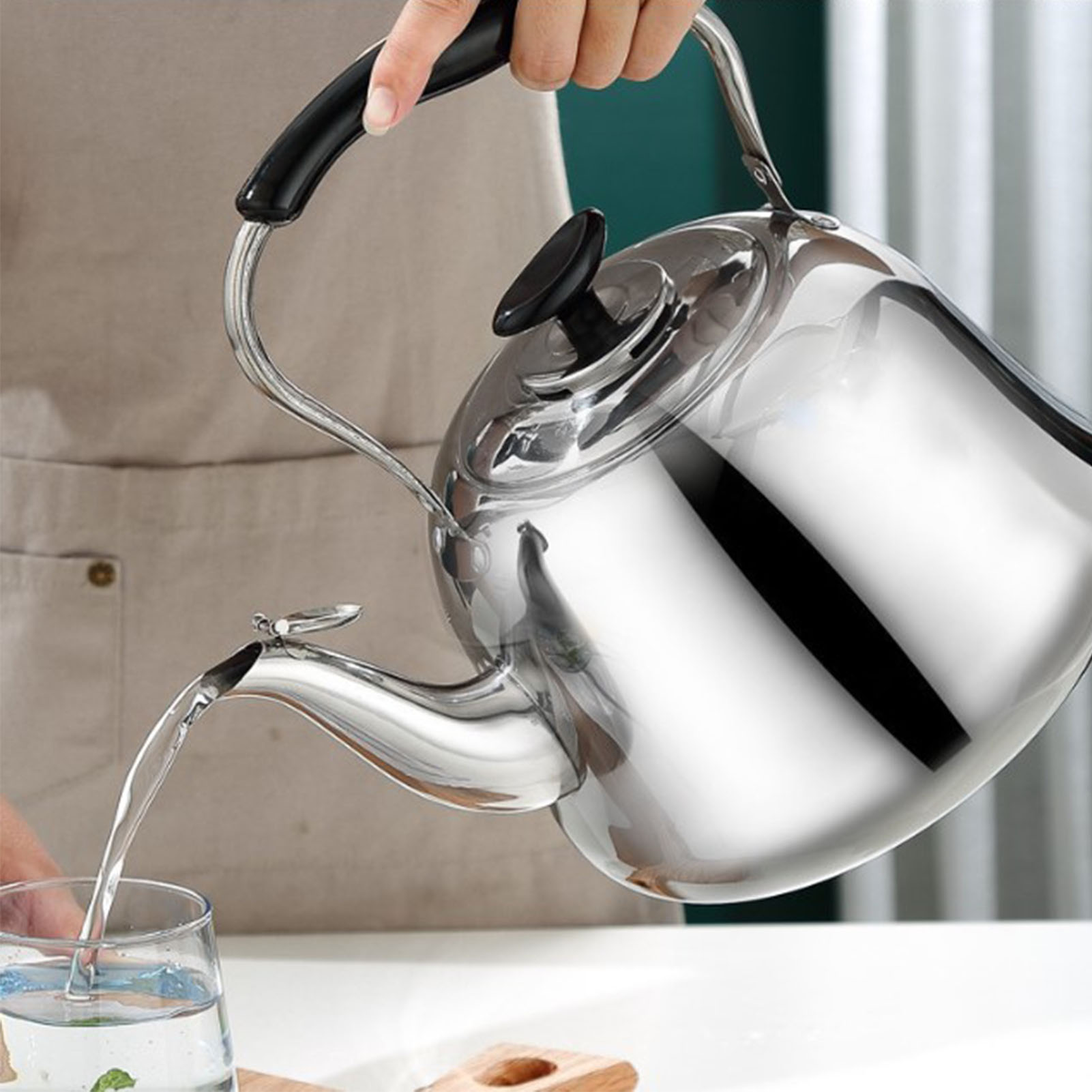 Eine Person gießt Wasser aus einem glänzenden Edelstahlkessel in ein Glas. Der Wasserkocher wird am Griff gehalten.
