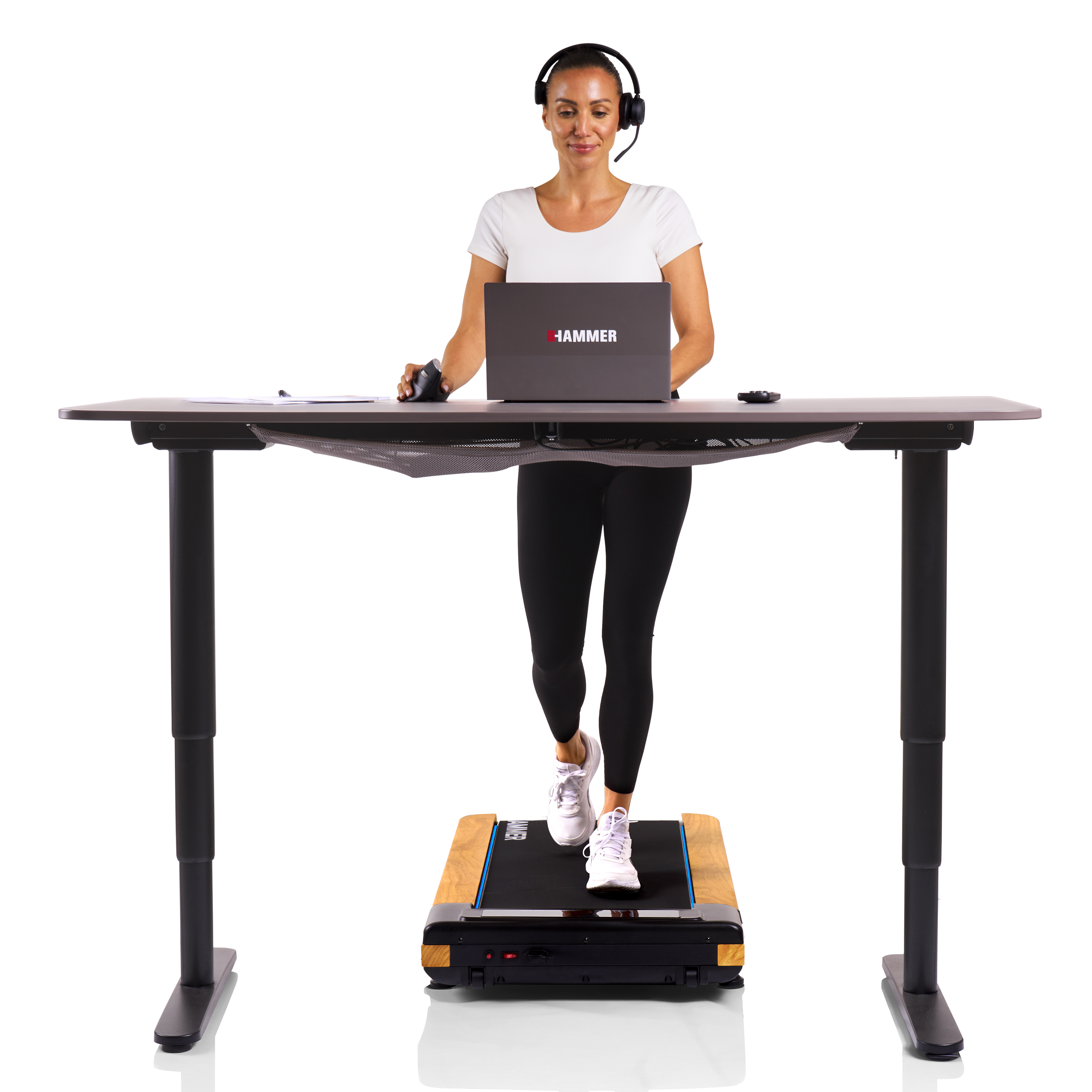 Frau arbeitet am Laptop, während sie auf einem Laufband-Schreibtisch geht. Sie trägt Kopfhörer und weiße Turnschuhe.