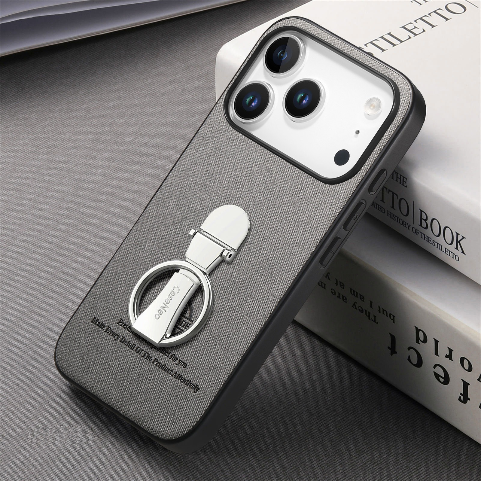 Una custodia per telefono con un anello d'argento su un libro. La custodia è grigia con bordo nero. Il libro ha pagine bianche.