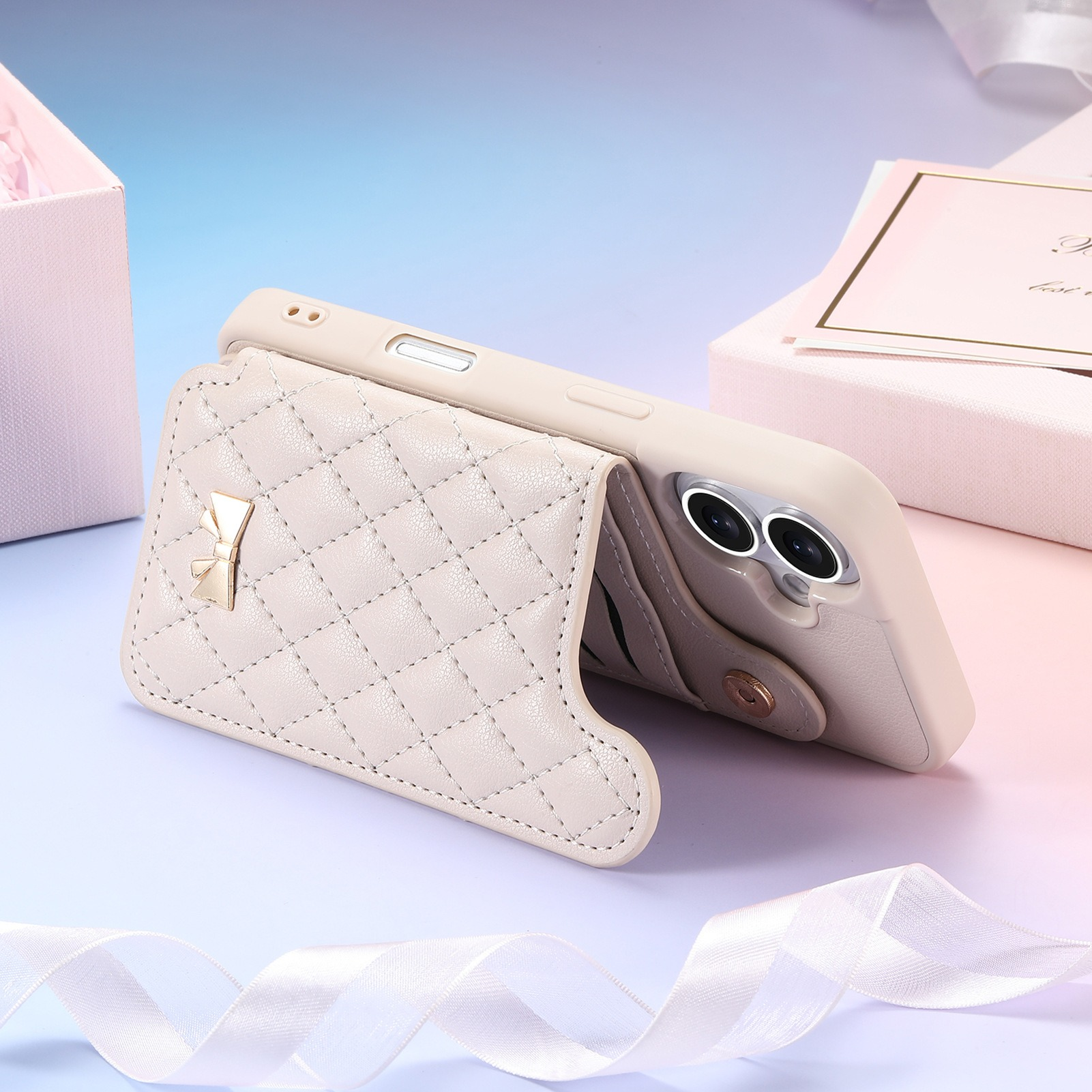 Beige Handyhülle mit goldener Schleife, geöffnet, um das Telefon mit zwei Kameras zu zeigen. Rosa Geschenkboxen und Karte im Hintergrund.