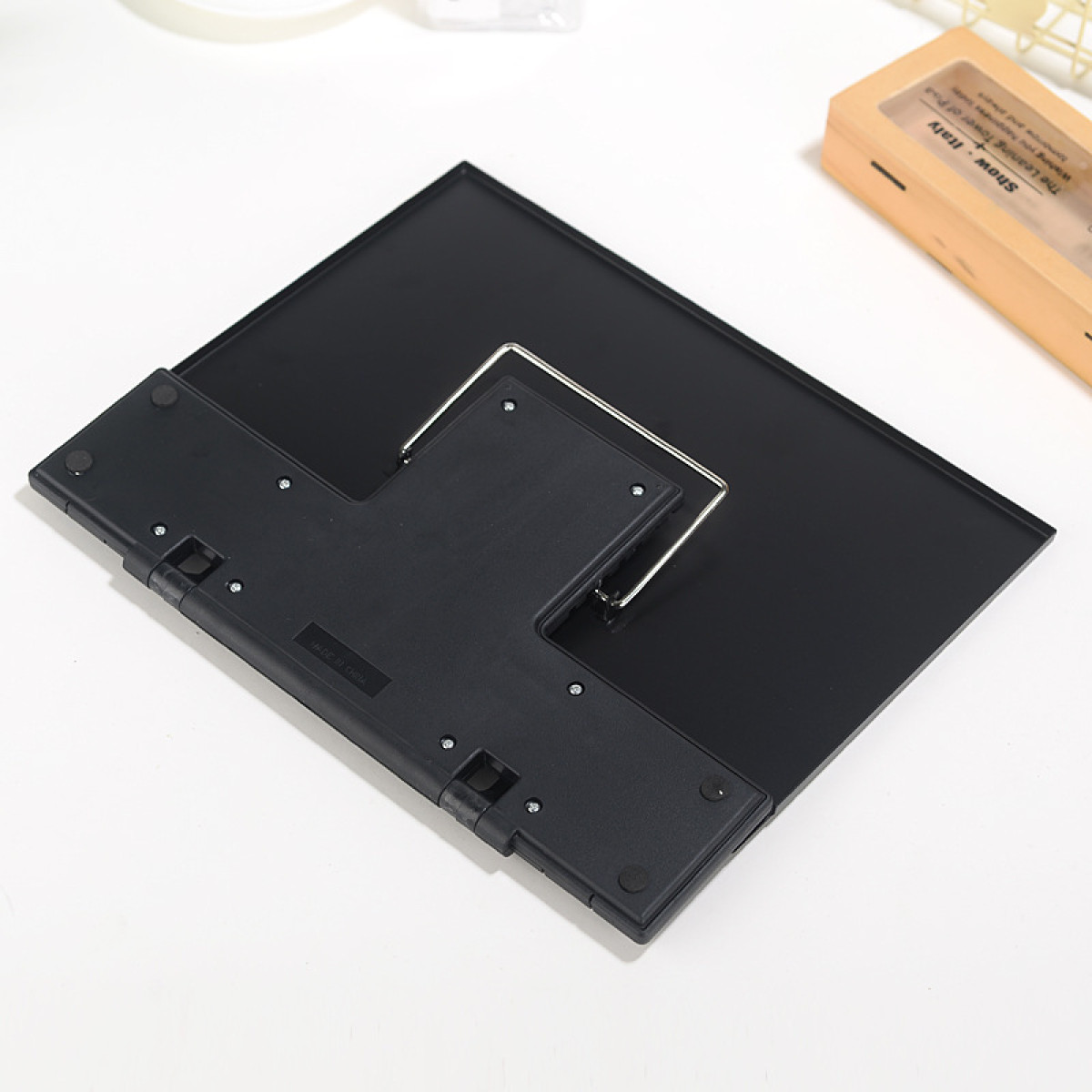 Czarny, kątowy stojak z metalową podporą na białej powierzchni. W tle widoczny jest beżowy pojemnik z tekstem.