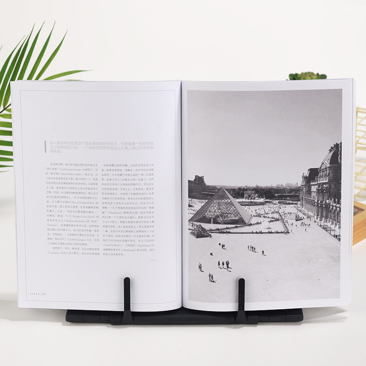 Książka z czarnym stojakiem, pokazująca czarno-białe zdjęcie Piramidy w Luwrze i ludzi.