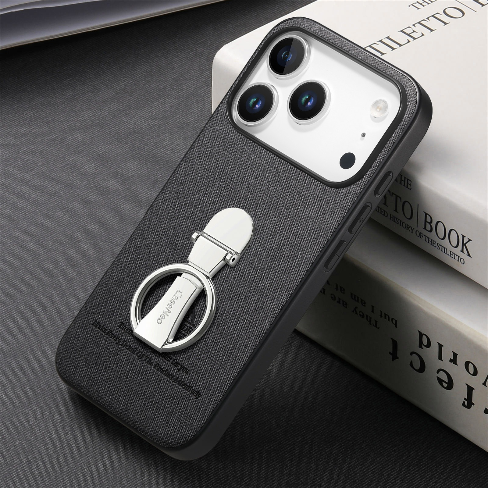 Una custodia nera con anello argentato su un libro. Il telefono ha tre fotocamere.