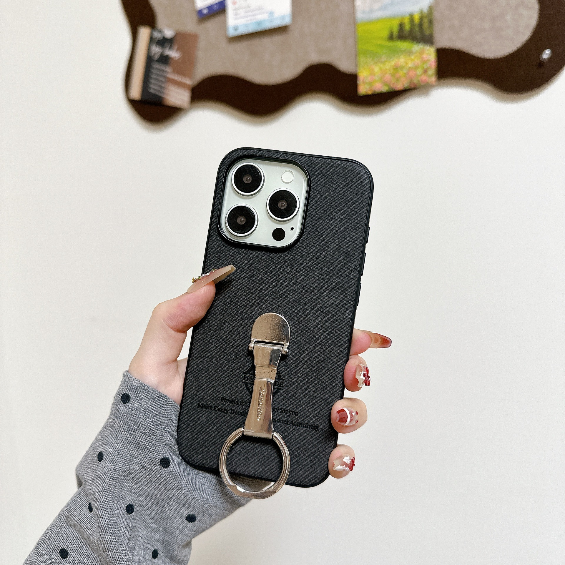 Una mano tiene un telefono con un portanello. Lo sfondo mostra una lavagna con appunti e un muro bianco.