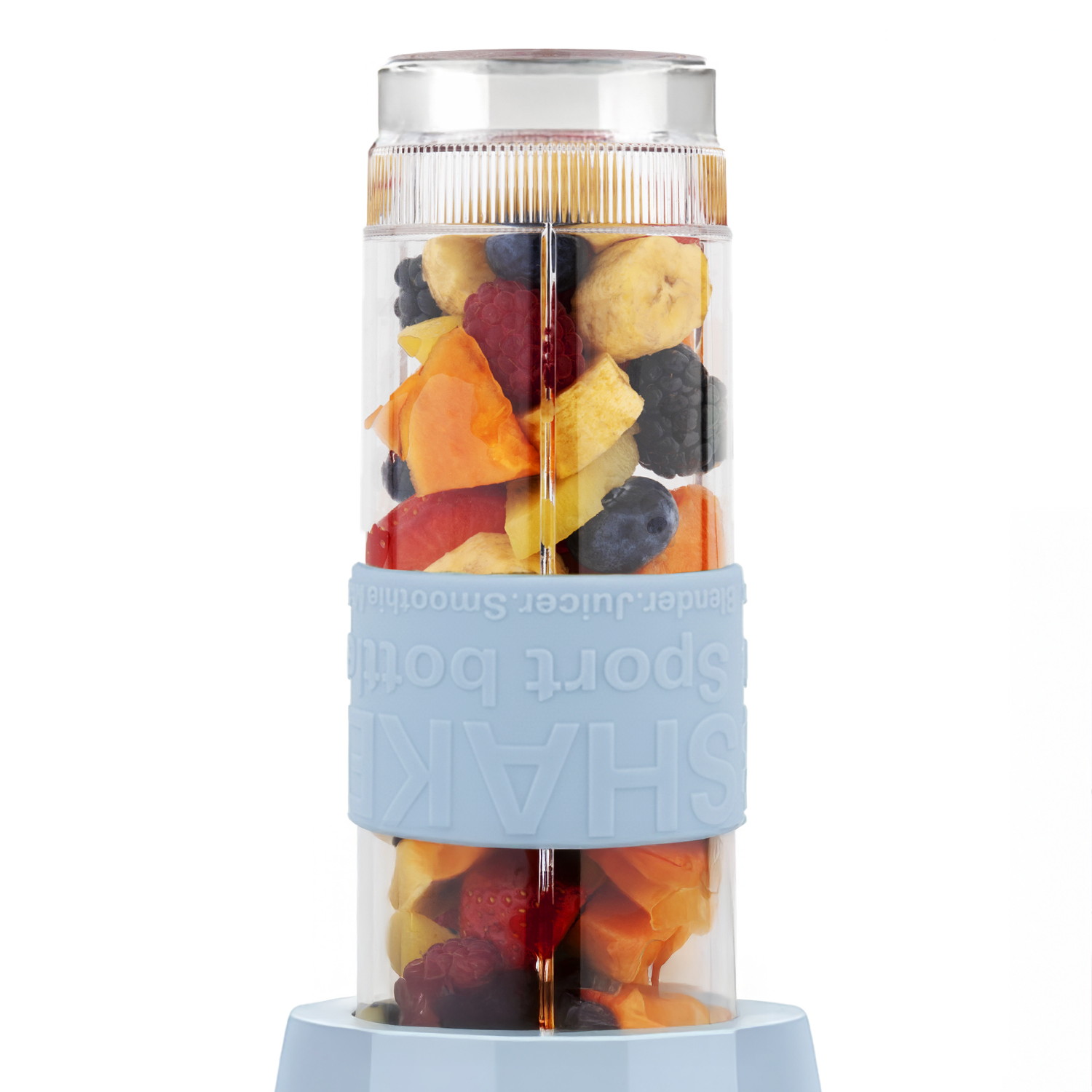 Una bottiglia frullatore trasparente piena di vari frutti come bacche, banane e papaya, con una fascia blu che dice 'SHAKE sport bottle'.