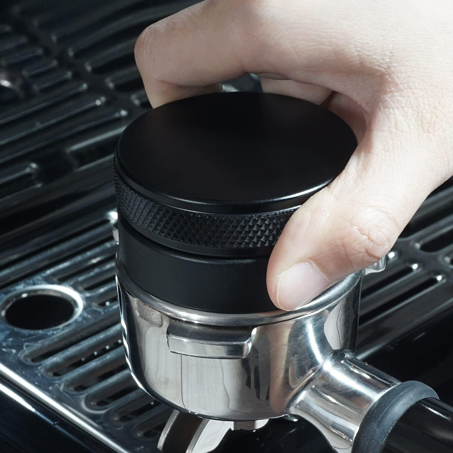 Eine Hand hält einen schwarzen Deckel auf einem verchromten Espressomaschinen-Siebträger. Die Maschine steht auf einer glänzenden, schwarzen Oberfläche.