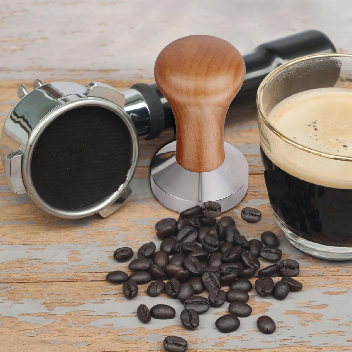 Kaffee-Setup: Tamper, Siebträger, Bohnen und Espresso in einem Glas auf Holz. Werkzeuge zur Kaffeezubereitung sind vorhanden.