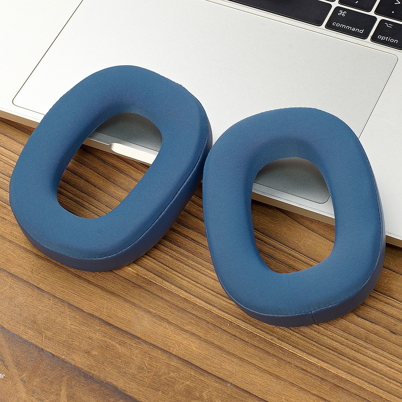 Two blue ear pads for headphones lie on a wooden surface next to a laptop.