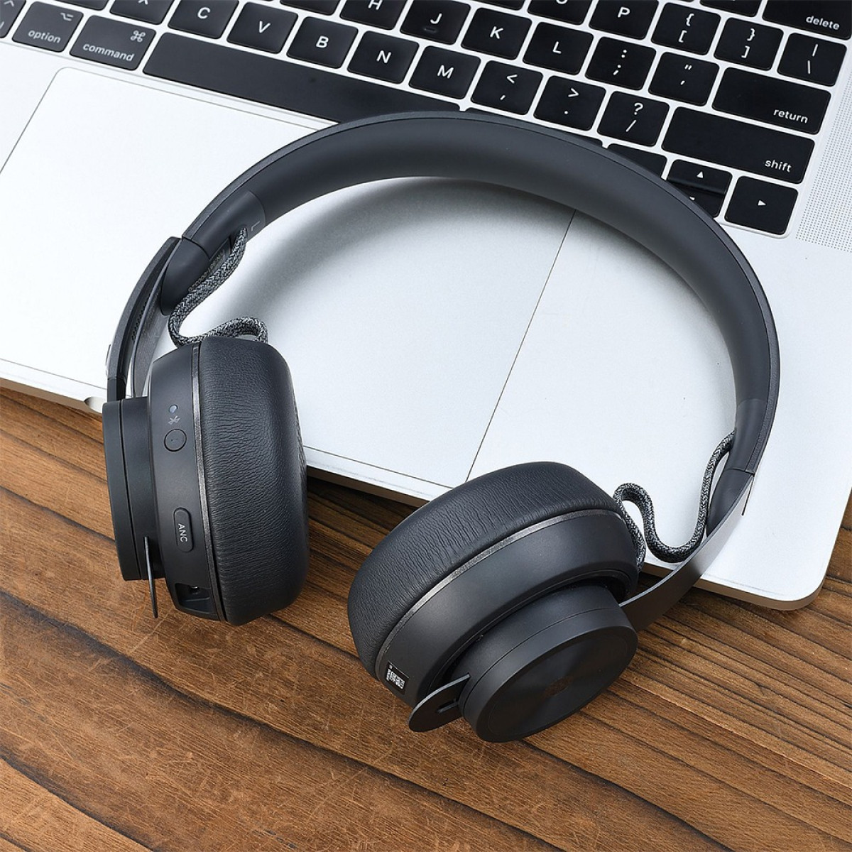 Cuffie nere su tastiera di laptop e superficie in legno. Le cuffie sono a fuoco, con pulsanti visibili sul padiglione sinistro.
