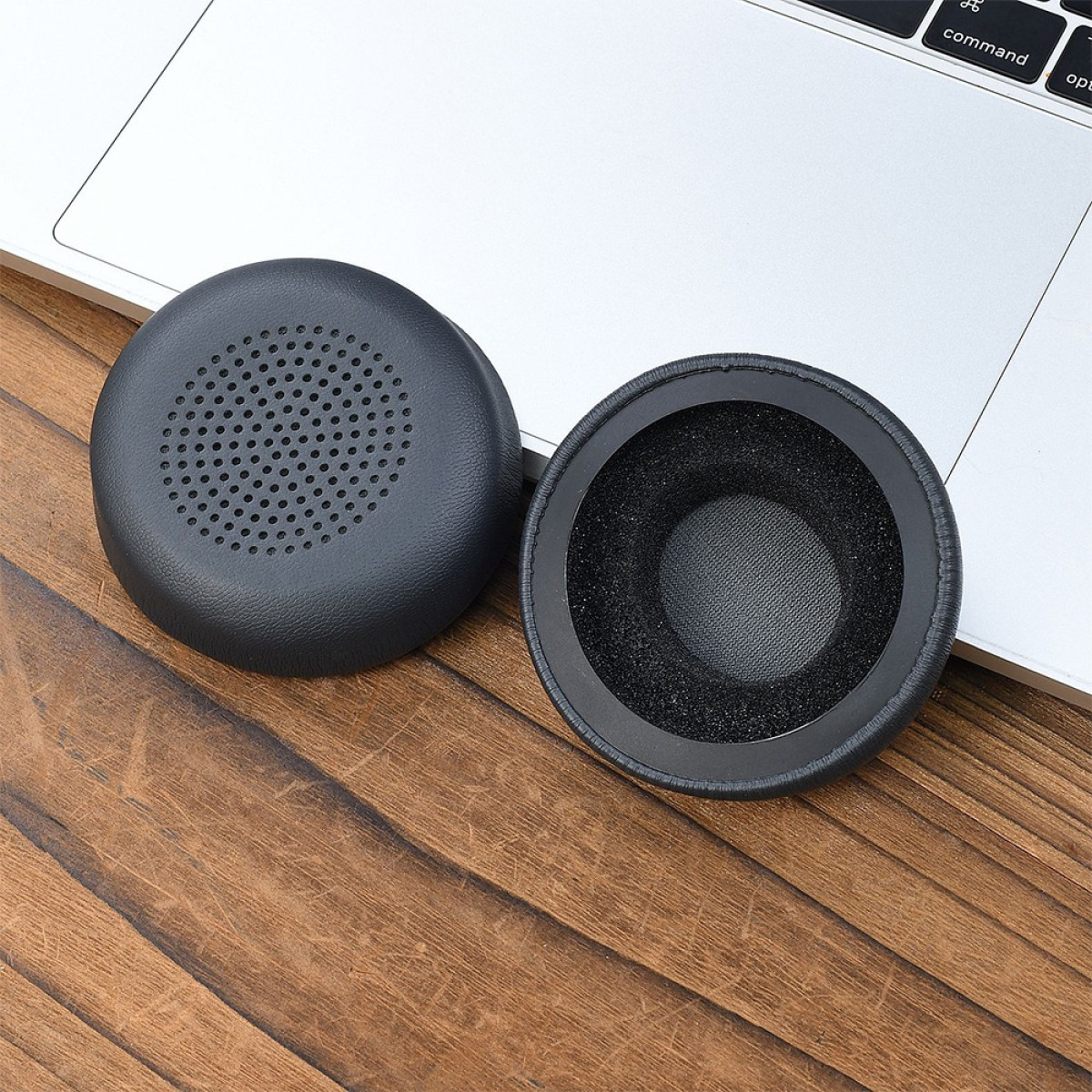 Due cuscinetti neri per cuffie su legno, accanto a una tastiera di un laptop. Uno ha fori, l'altro un interno in schiuma.