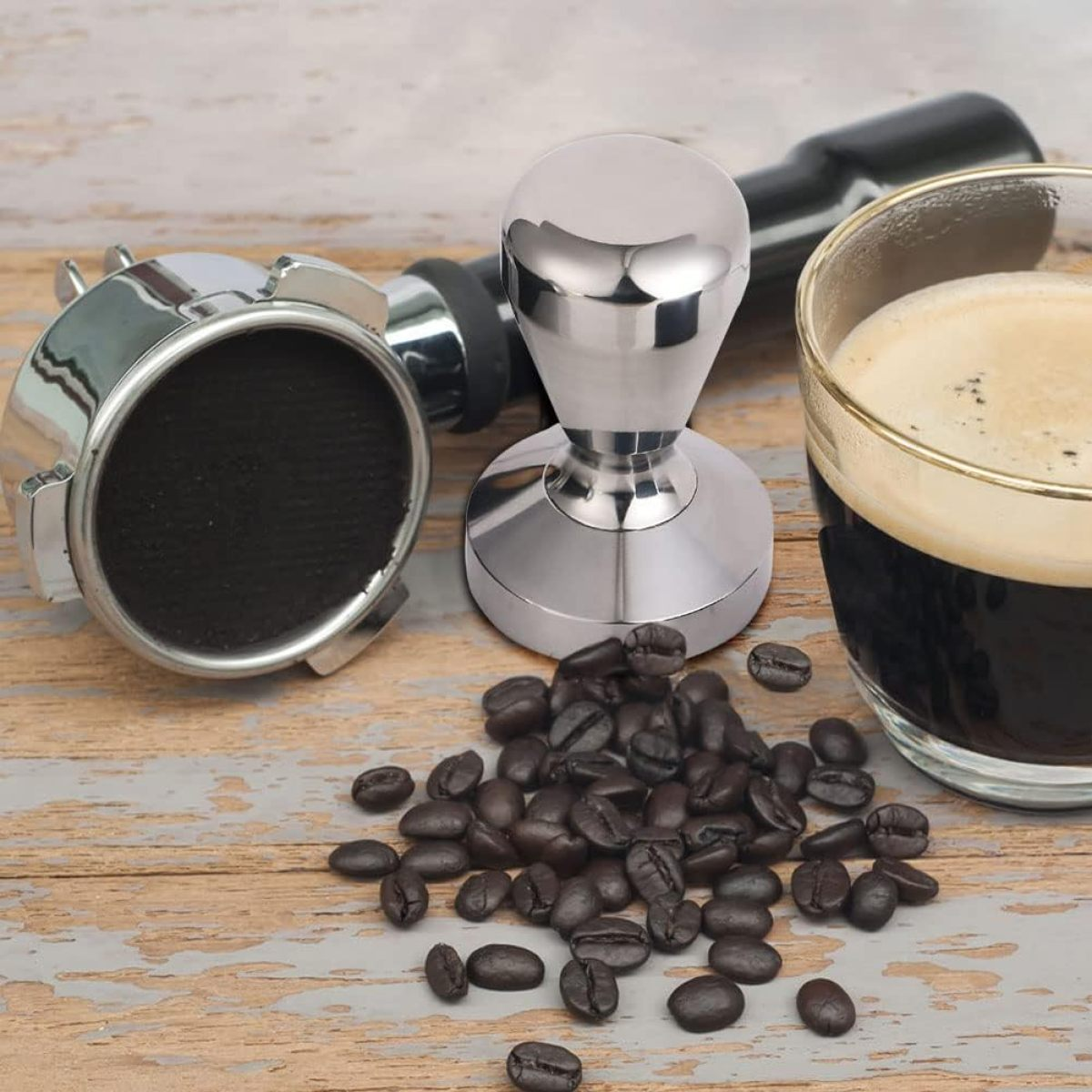 Kaffee-Setup. Enthält einen Siebträger, einen Tamper, ein Glas Kaffee und Kaffeebohnen auf einer Holzoberfläche.