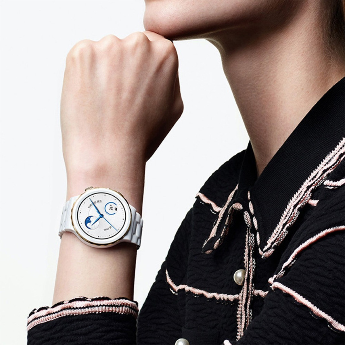 Eine Person trägt eine weiße Smartwatch. Die Person trägt ein schwarzes Hemd mit rosa Akzenten. Die Uhr zeigt Uhrzeit und Mondphase an.