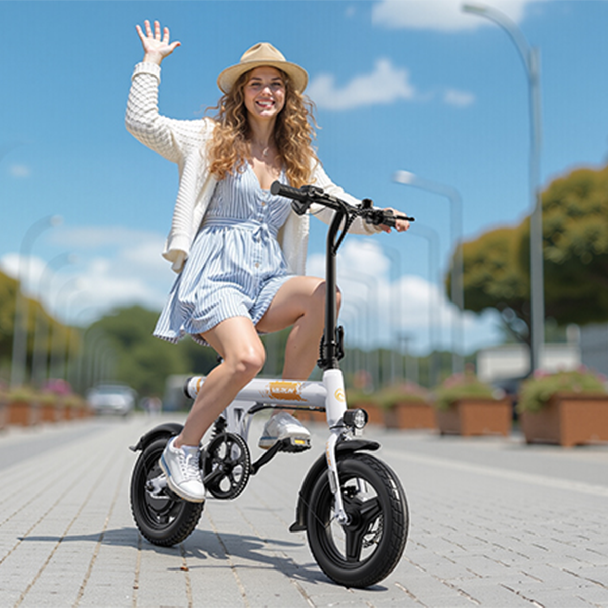 Kobieta macha, jadąc biało-czarnym rowerem elektrycznym po utwardzonej drodze. Ma na sobie kapelusz, sukienkę i sweter.