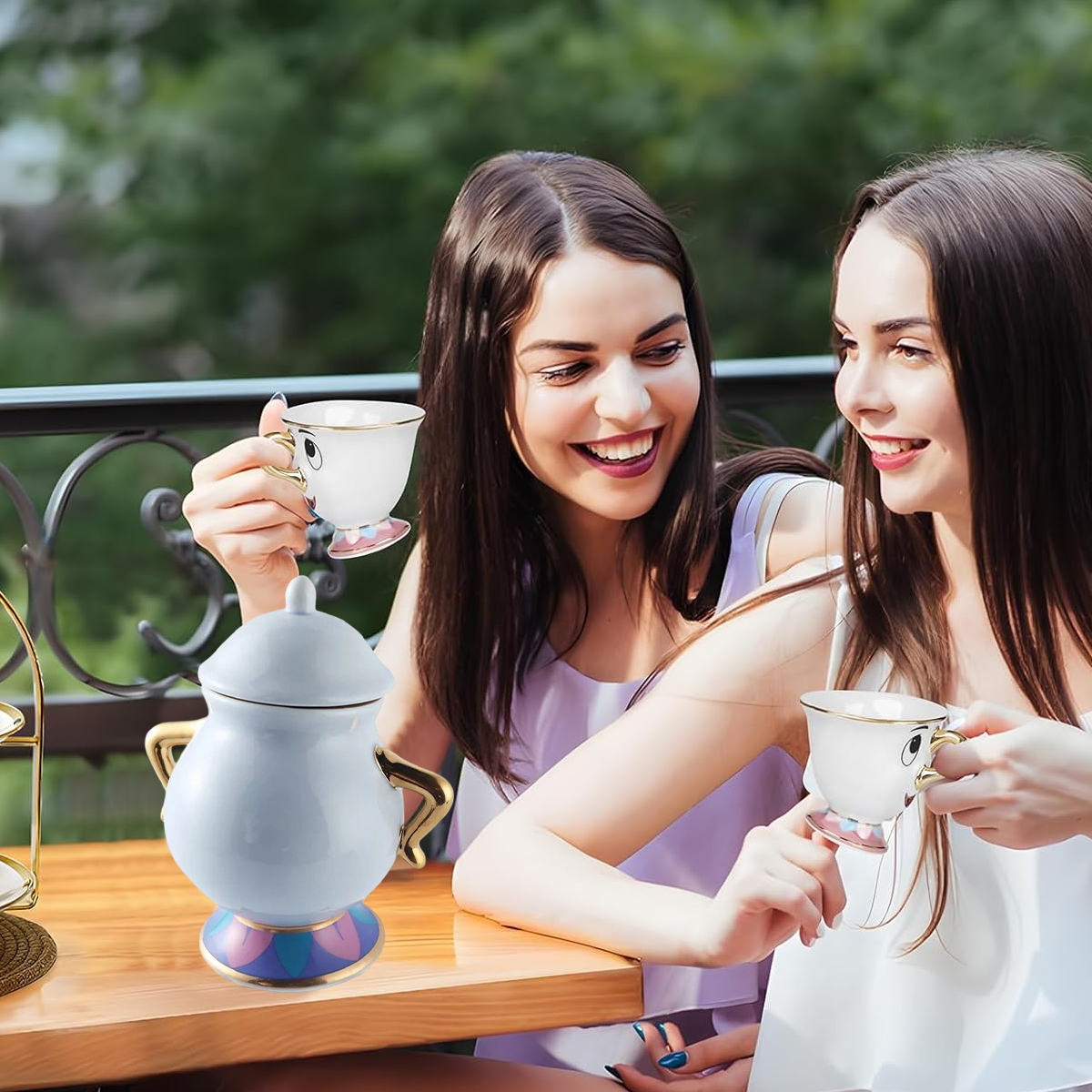 Zwei lächelnde Frauen halten Teetassen und sitzen an einem Tisch mit einer Teekanne. Der Hintergrund ist verschwommenes grünes Laub und ein Balkon.