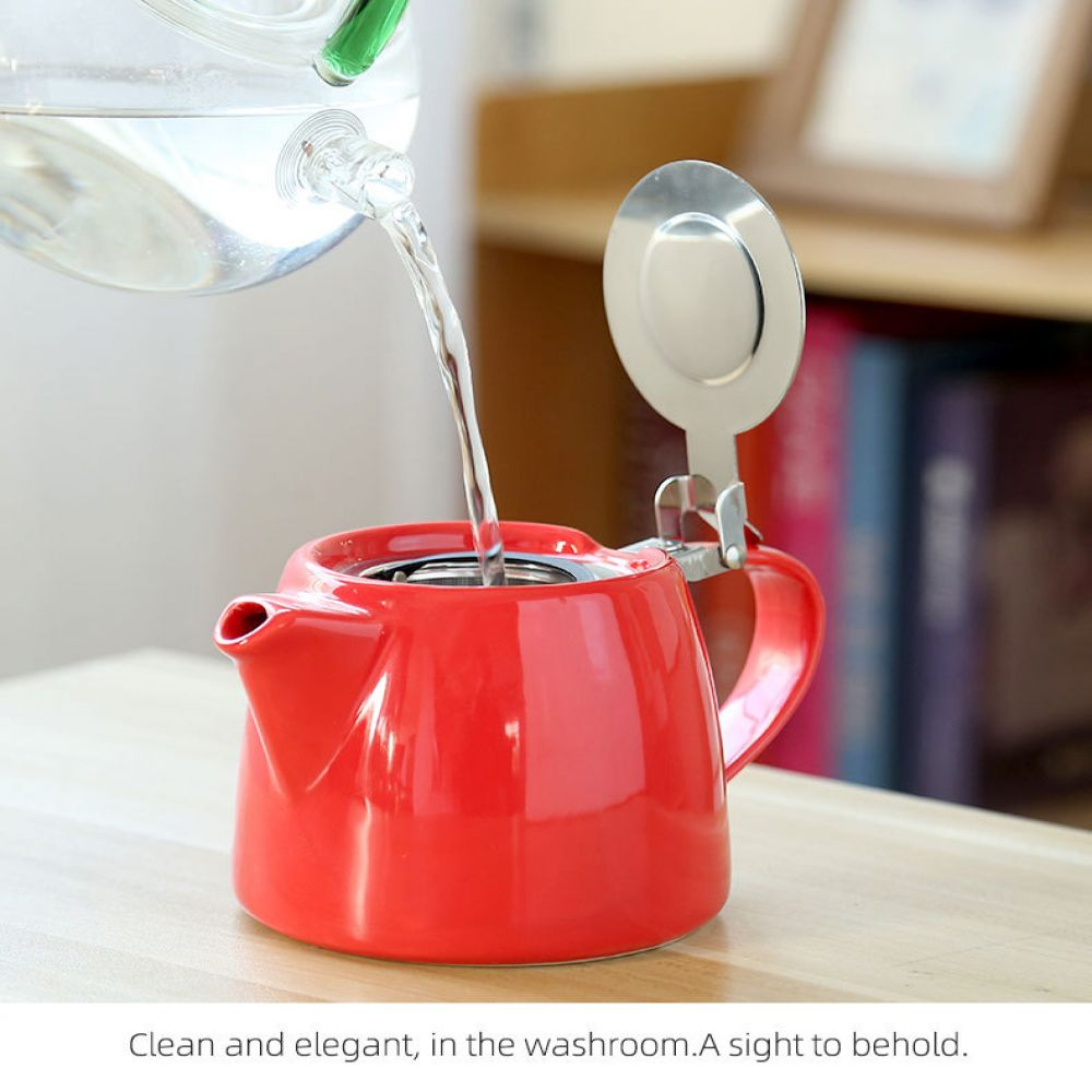 Eine rote Teekanne wird mit Wasser aus einem durchsichtigen Glaskessel gefüllt. Ein silberner Deckel ist an der Teekanne befestigt. Der Hintergrund ist unscharf.
