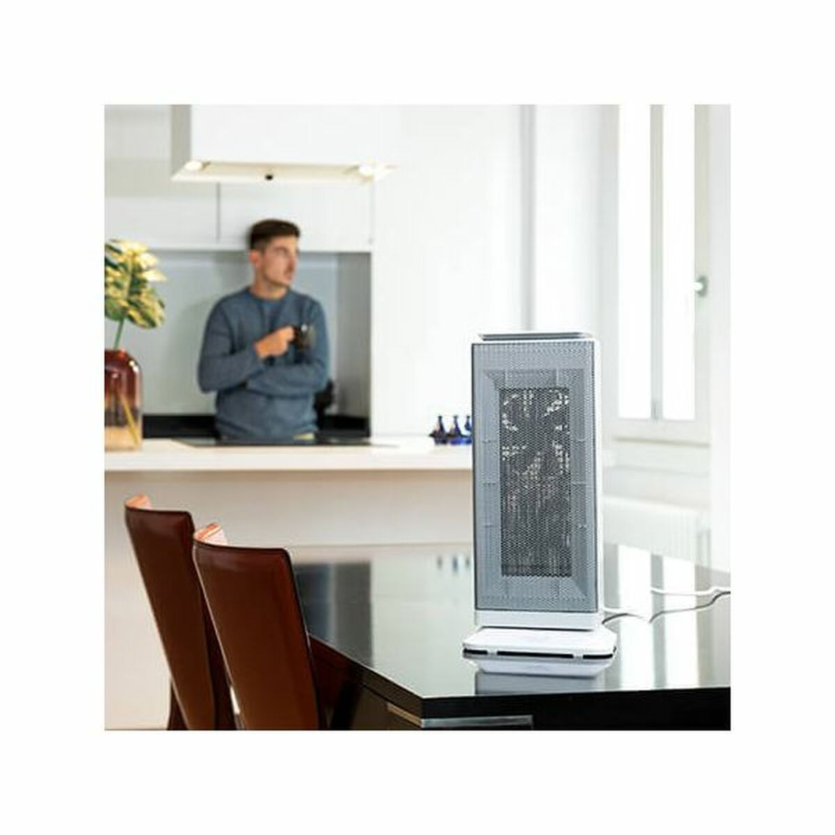 Mężczyzna w niebieskiej koszuli stoi blisko białej kuchni. Biało-szary grzejnik stoi na czarnym stole z brązowymi krzesłami.