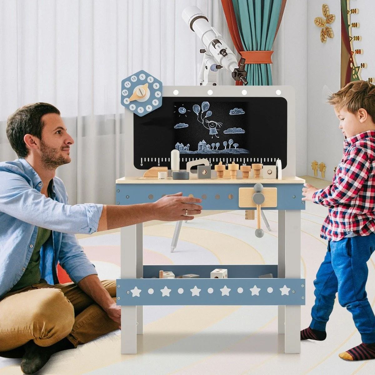 Un hombre y un niño están cerca de un banco de trabajo para niños. El banco de trabajo tiene herramientas y una pizarra. Un telescopio está al fondo.
