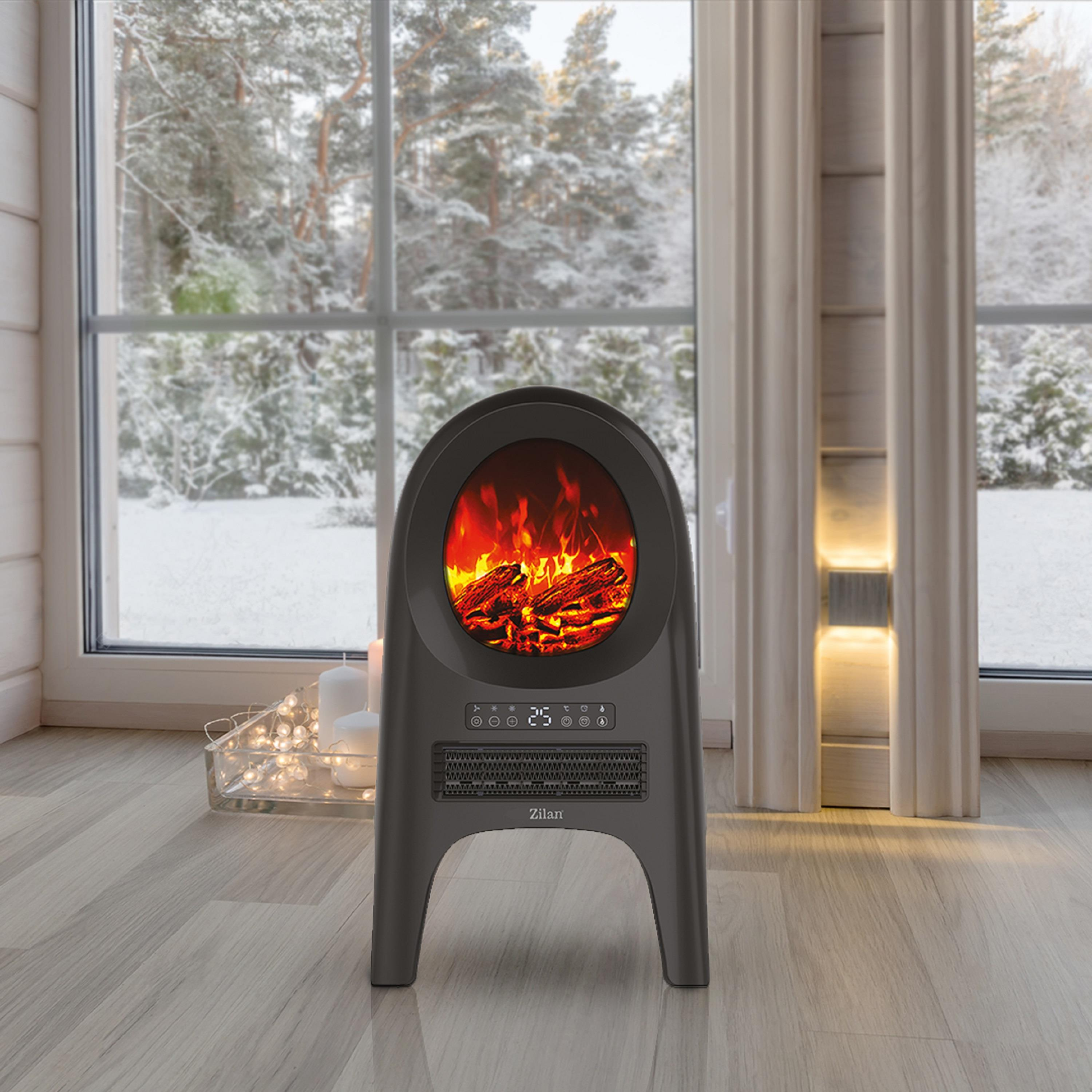 Ein dunkelgrauer Elektrokamin mit Flammeneffekt. Im Hintergrund ist ein verschneiter Wald durch ein Fenster zu sehen.