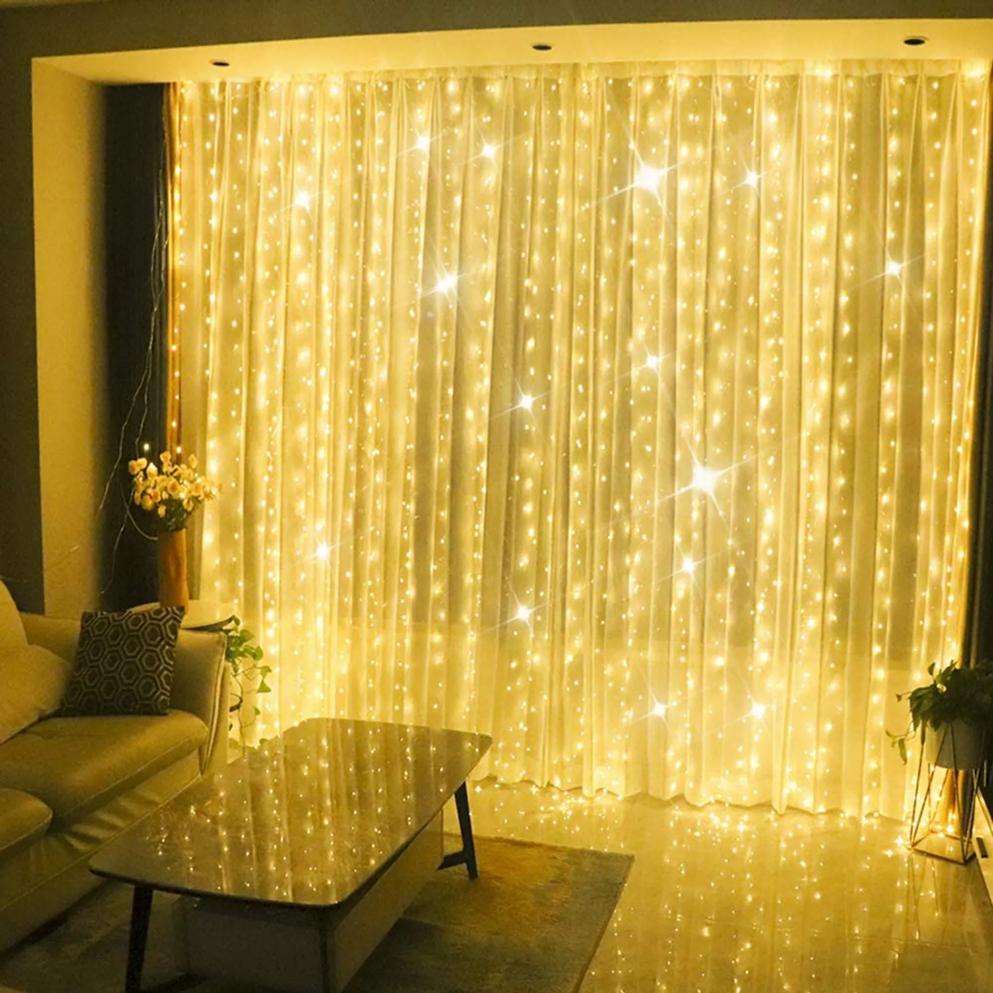 Ein Raum mit leuchtenden Lichterketten hinter transparenten Vorhängen. Sofa, Tisch und Pflanzen im Vordergrund.