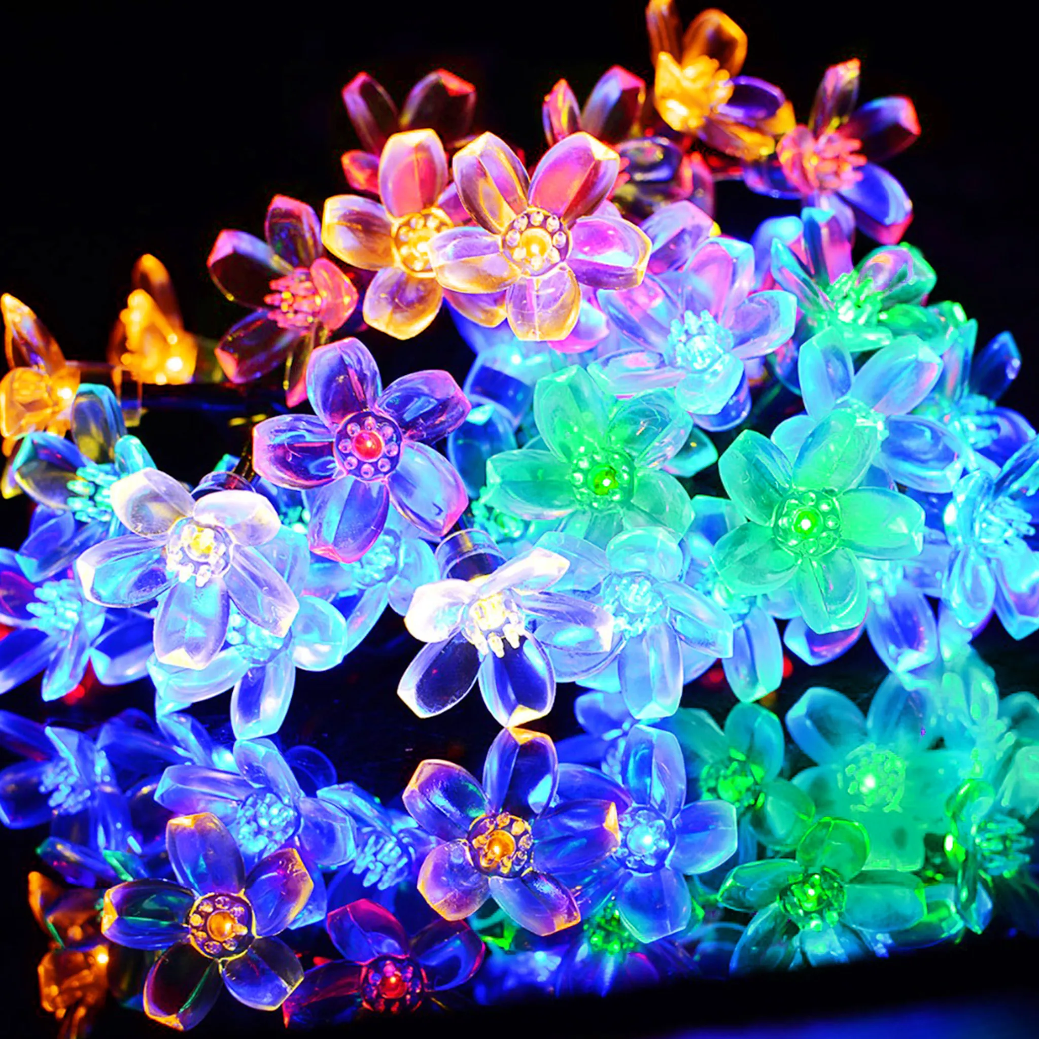 Nahaufnahme von bunten blütenförmigen Lichtern vor schwarzem Hintergrund. Die Lichter sind blau, grün, gelb und rot.