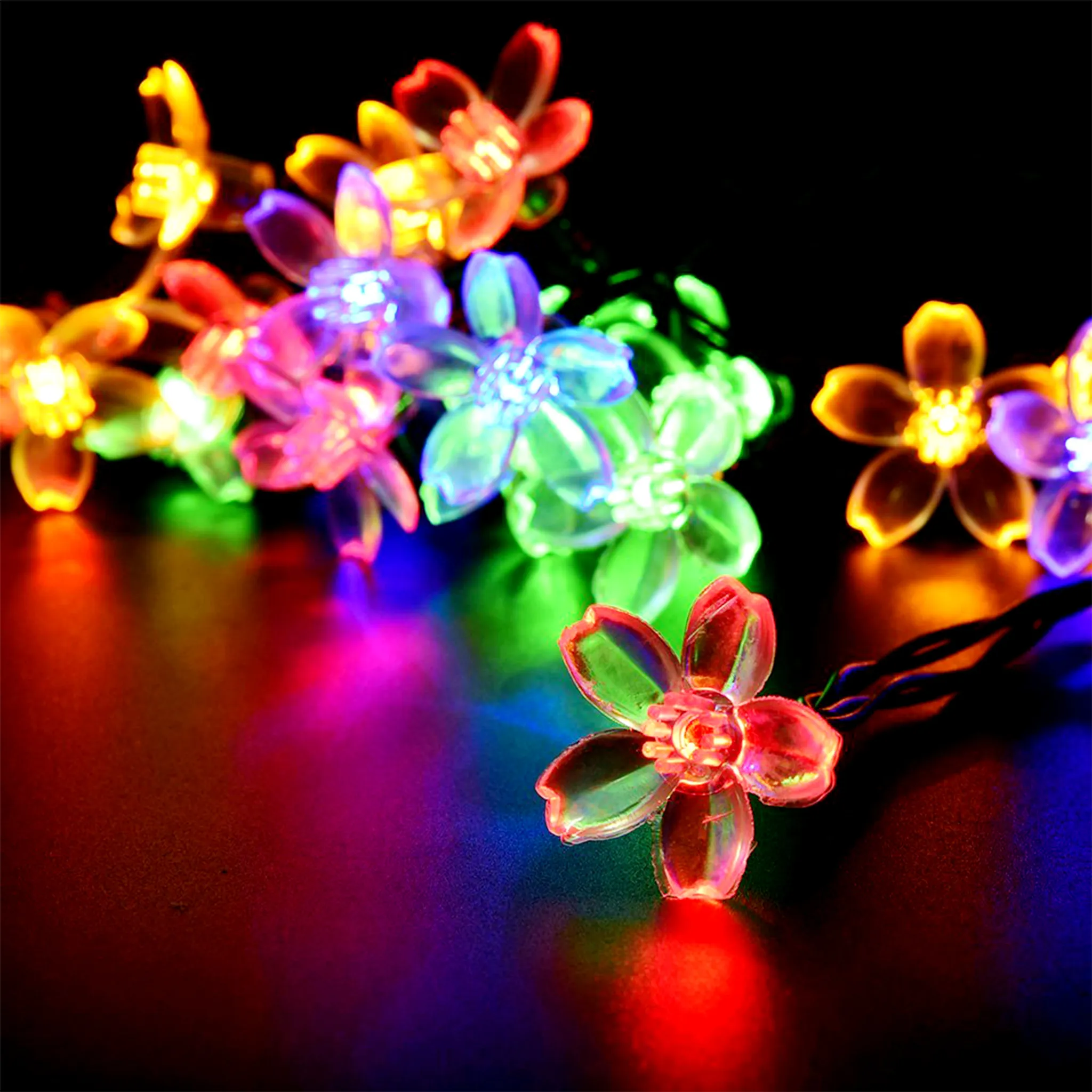 Nahaufnahme von Lichterketten in Blumenform, verschiedenen Farben, auf dunkler Oberfläche. Schwarzer Hintergrund mit Farbreflexionen.