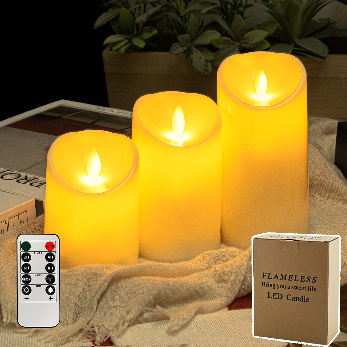 Drei flammenlose LED-Kerzen leuchten. Eine Fernbedienung und eine Schachtel befinden sich davor. Der Hintergrund hat Pflanzen und ein Buch.