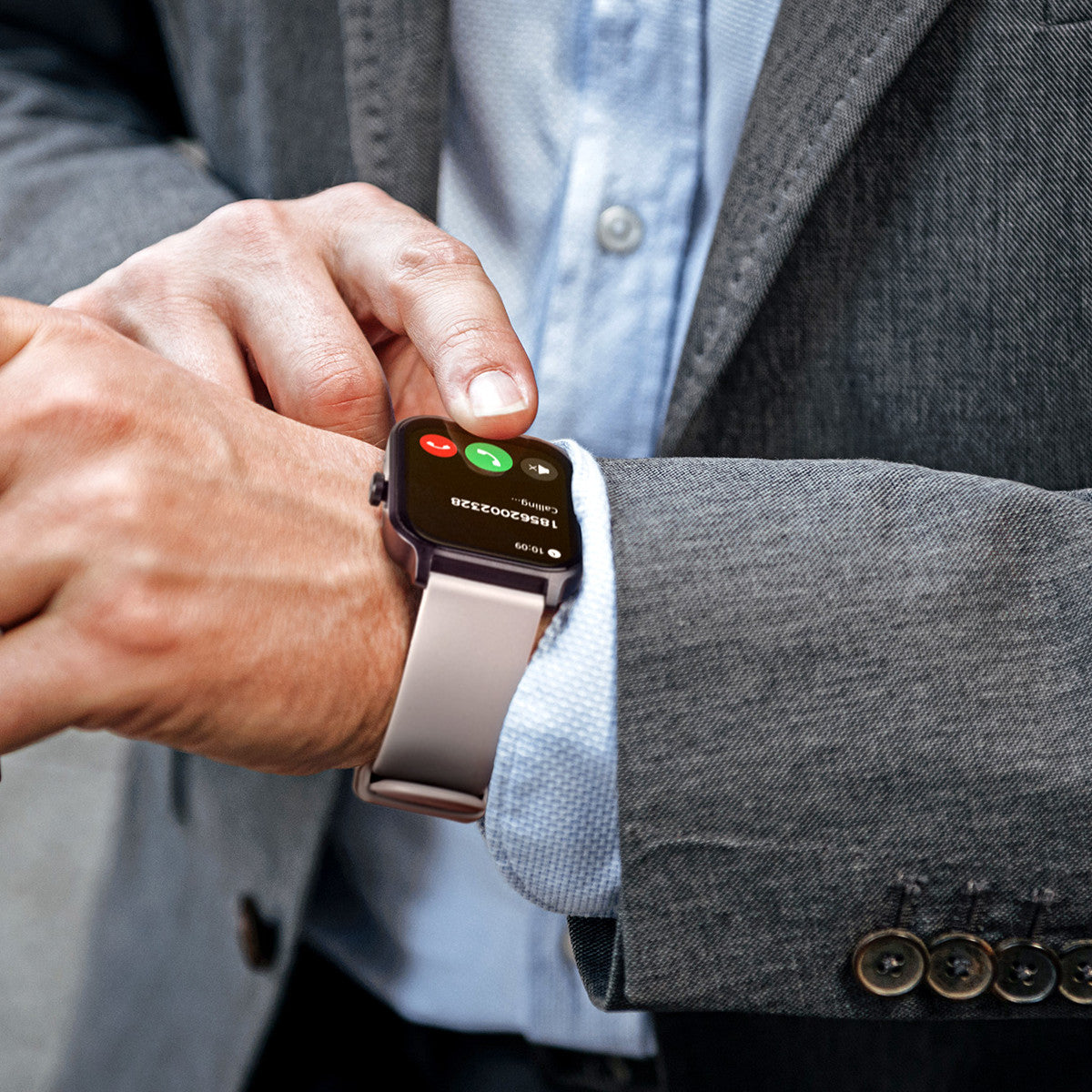 Un uomo in giacca e cravatta guarda uno smartwatch. L'orologio mostra una schermata di chiamata con pulsanti rossi e verdi.