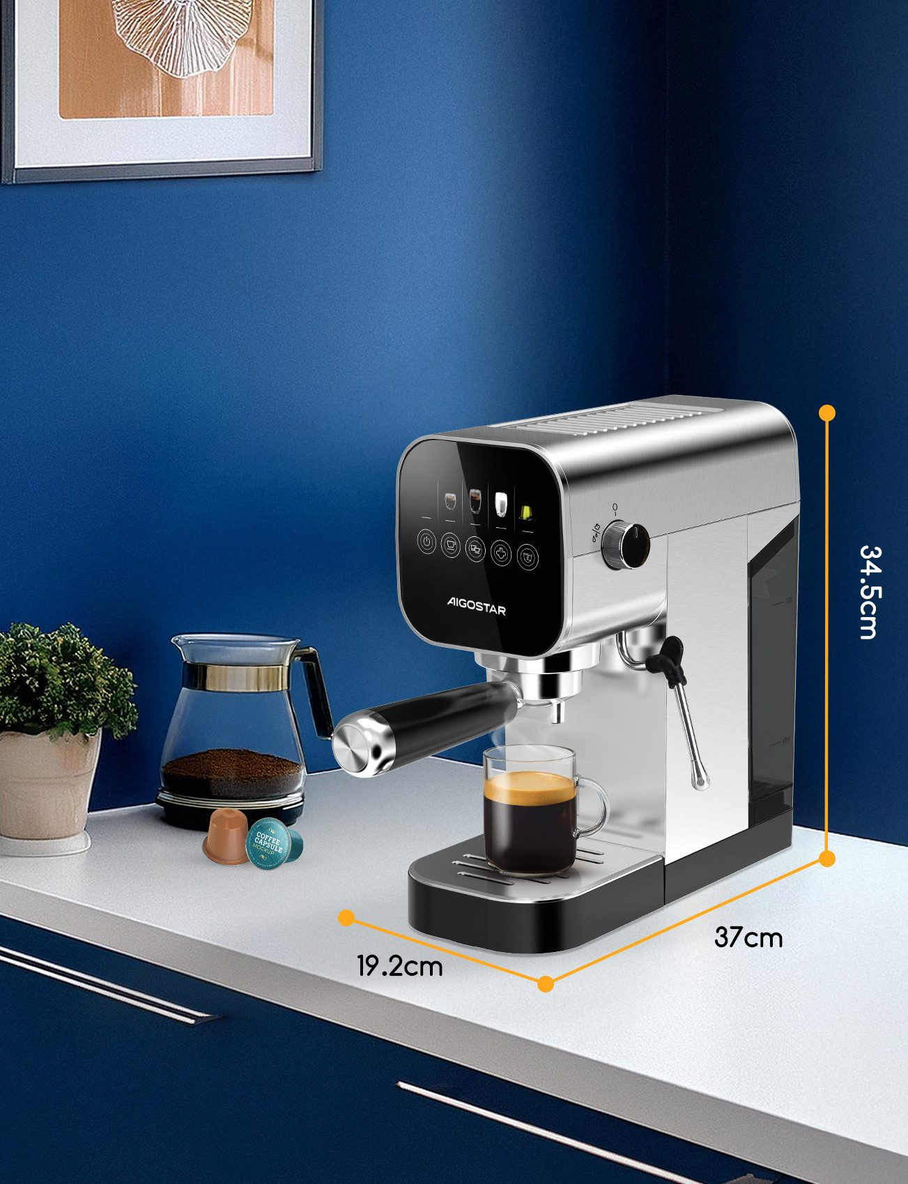 Eine silber-schwarze Espressomaschine mit einer Tasse Kaffee. Daneben befinden sich eine Glaskaraffe, Kapseln und eine kleine Pflanze.