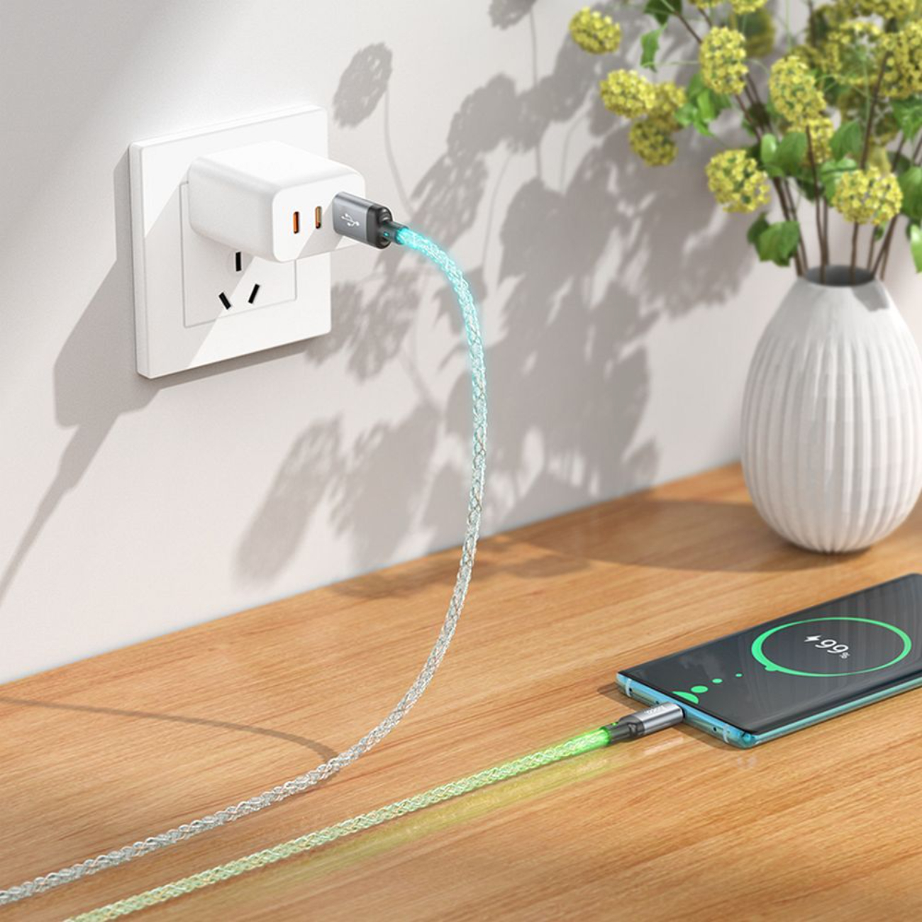 Un telefono in carica con un cavo luminoso. Il telefono è su una superficie di legno. Un vaso di fiori sullo sfondo.