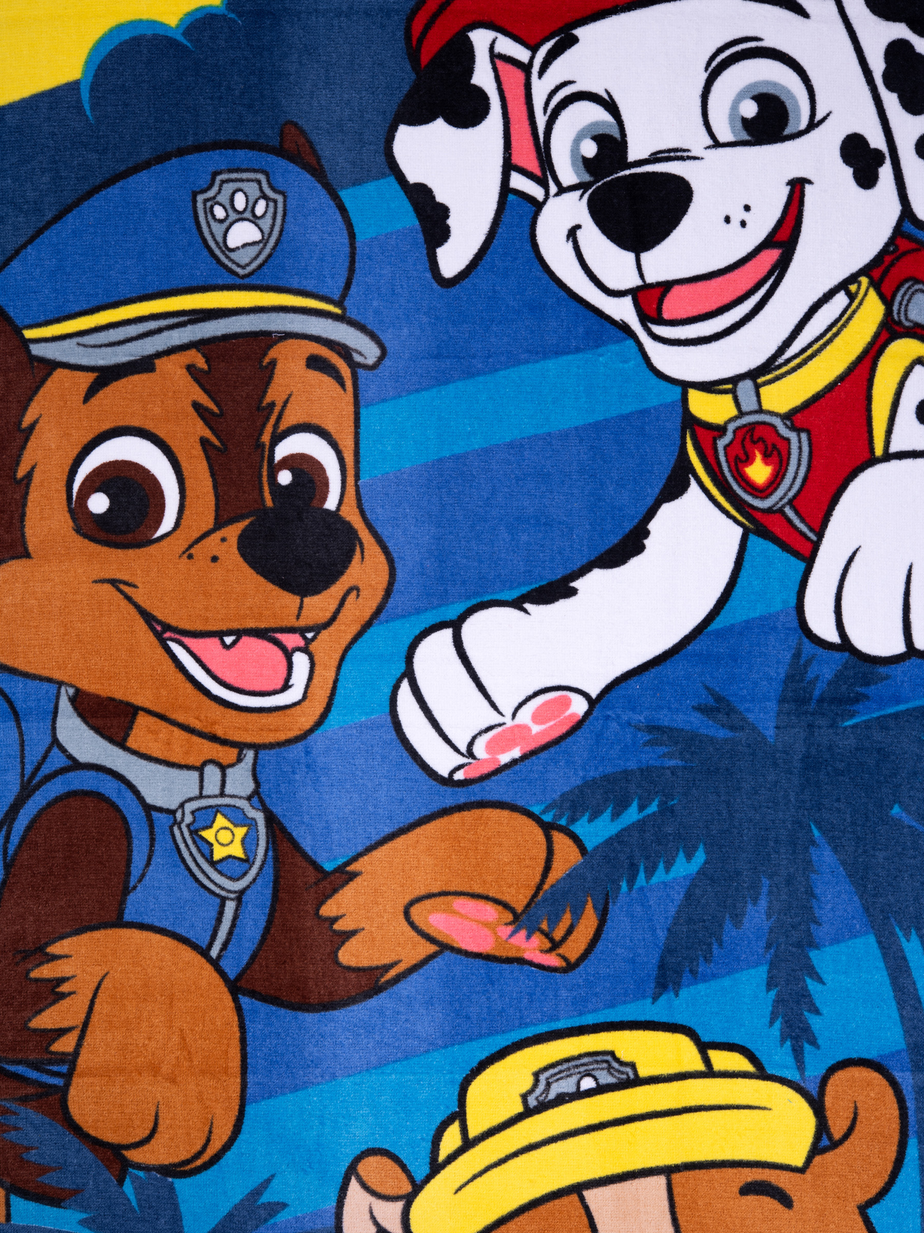 Paw Patrol Handtuch mit Chase, Marshall und Zuma. Blauer Hintergrund mit Palmen und gelbem Himmel.