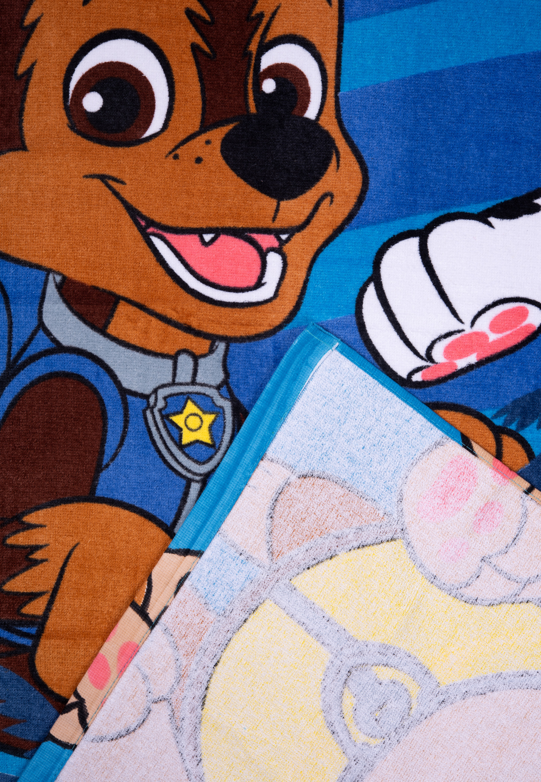 Handtuch mit Cartoon-Hunde-Gesicht, blau und braun. Ein Teil eines anderen Handtuchs ist sichtbar, mit Pfotenabdrücken.
