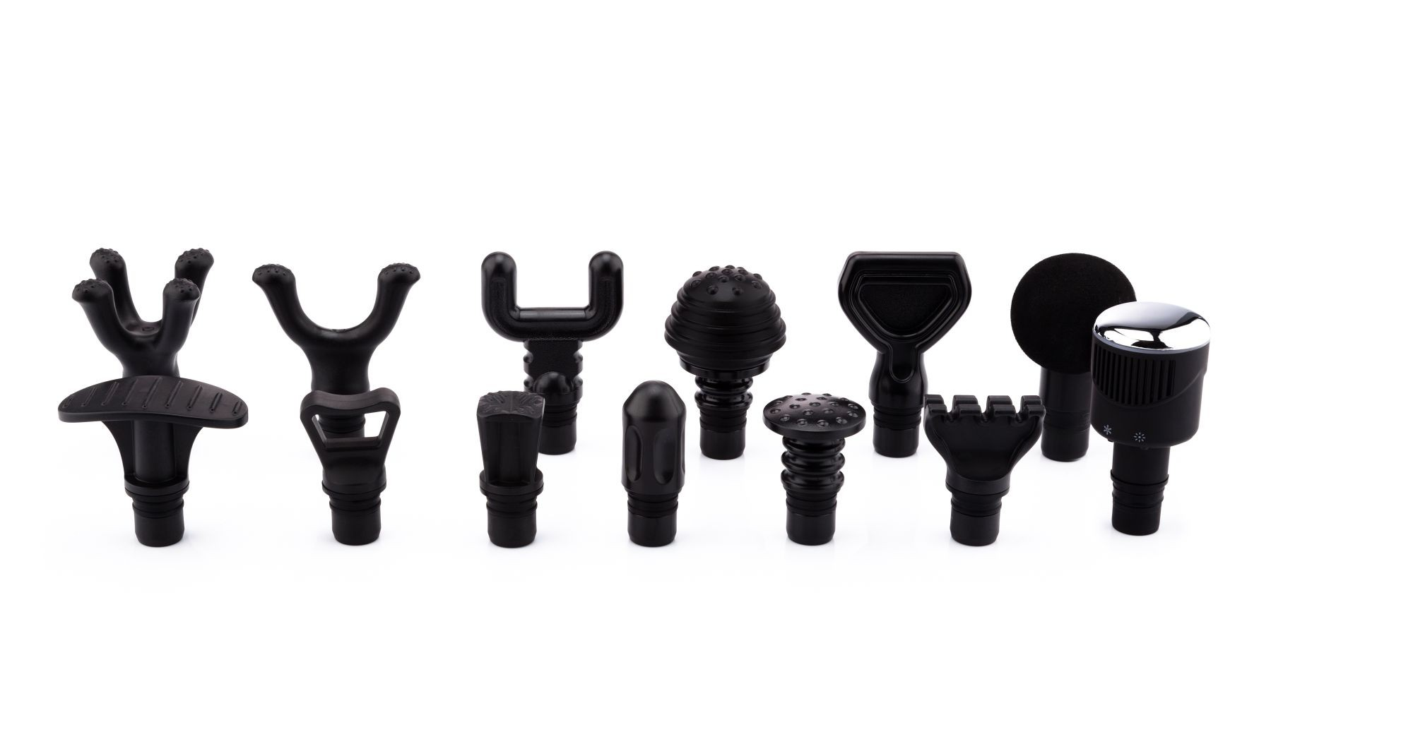 Divers accessoires noirs pour pistolet de massage disposés sur une surface blanche. Différentes formes et tailles sont visibles, tous noirs.