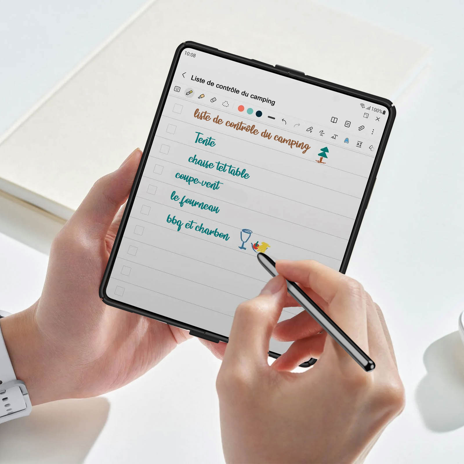 Une main tient une tablette affichant une liste de contrôle de camping. Un stylet survole l'écran. L'arrière-plan est flou.