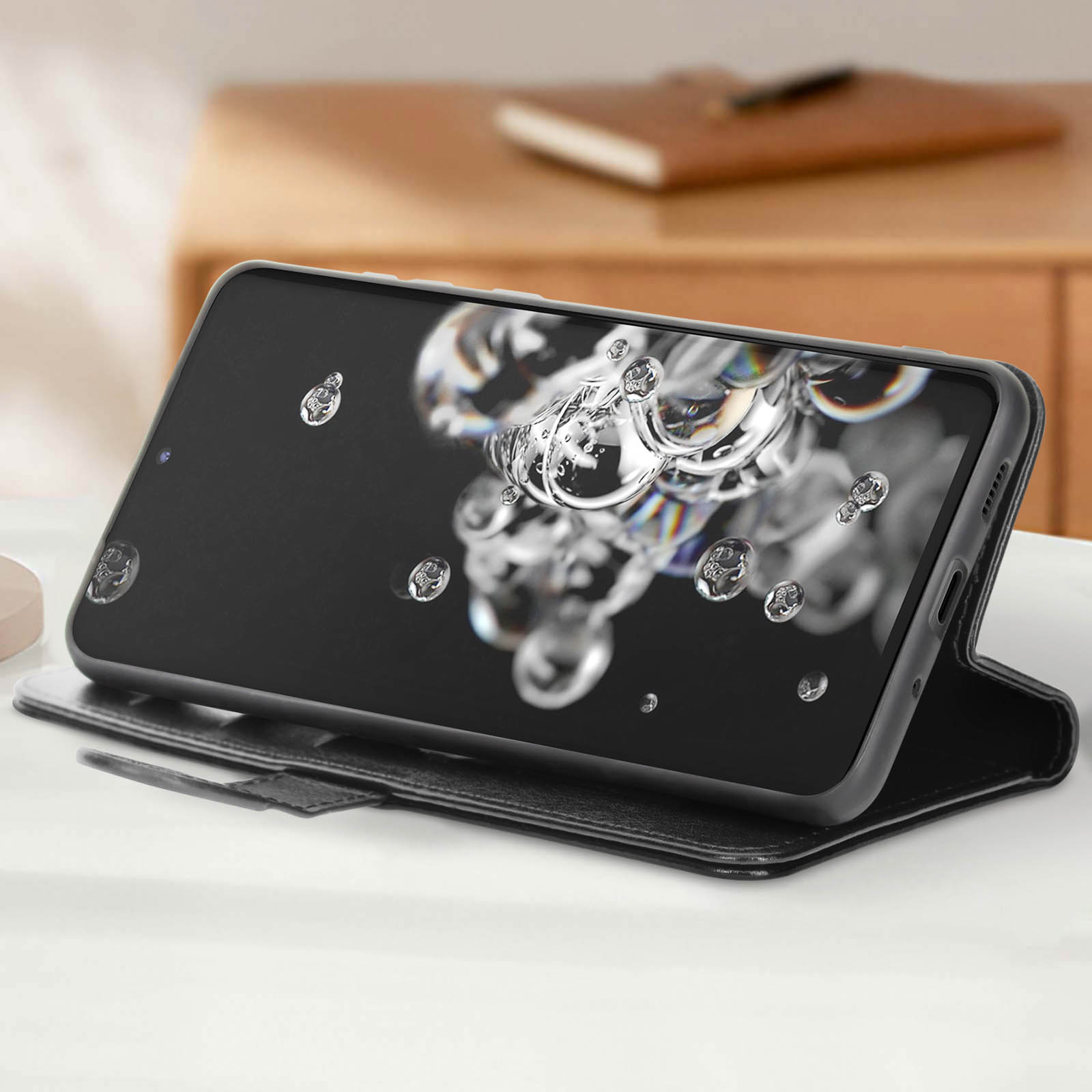 Een smartphone in een zwarte hoes toont een watereffect. Het staat op een witte tafel. Een boek staat op de achtergrond.