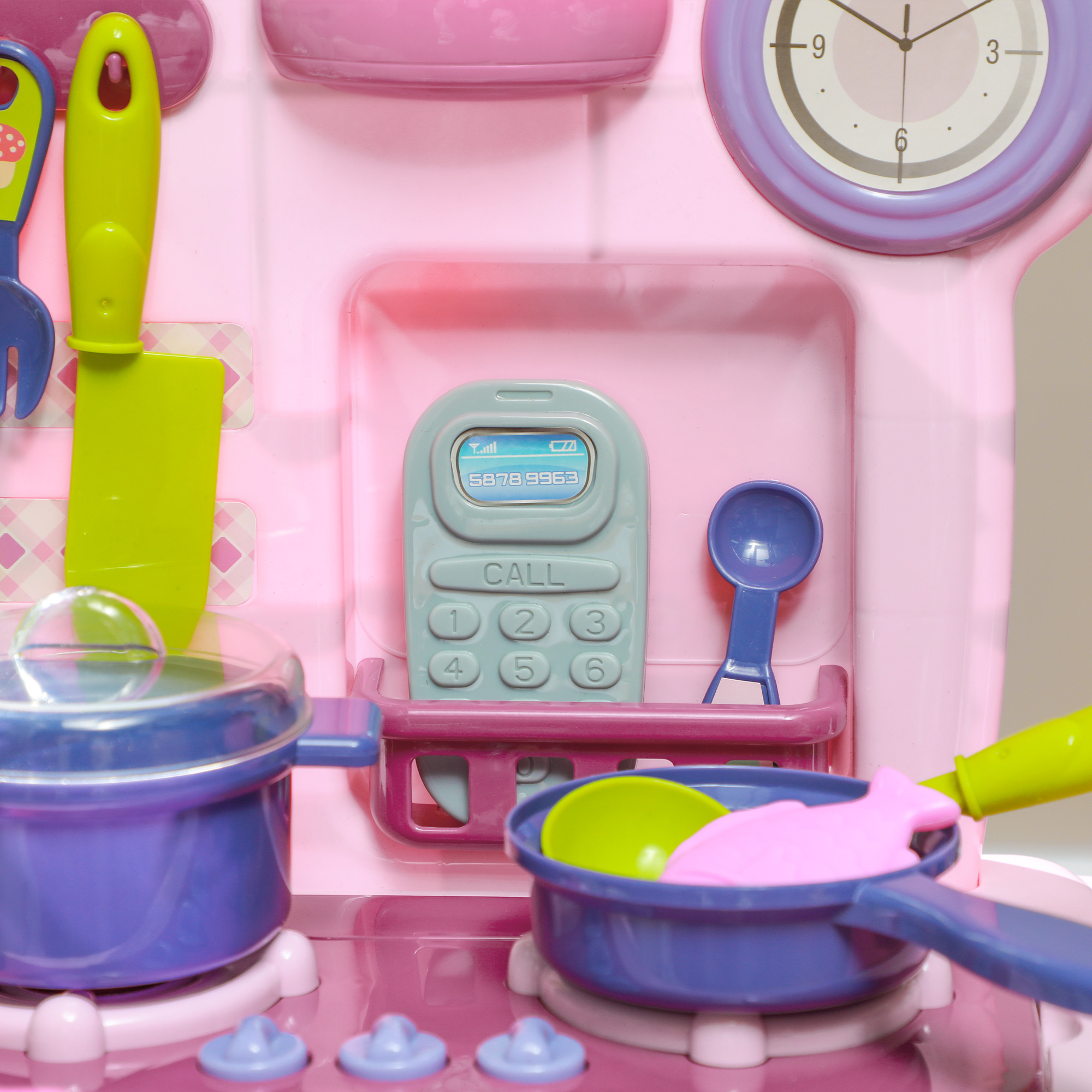 Una cucina giocattolo rosa con utensili, un telefono e un orologio. Padelle e pentole sul fornello.