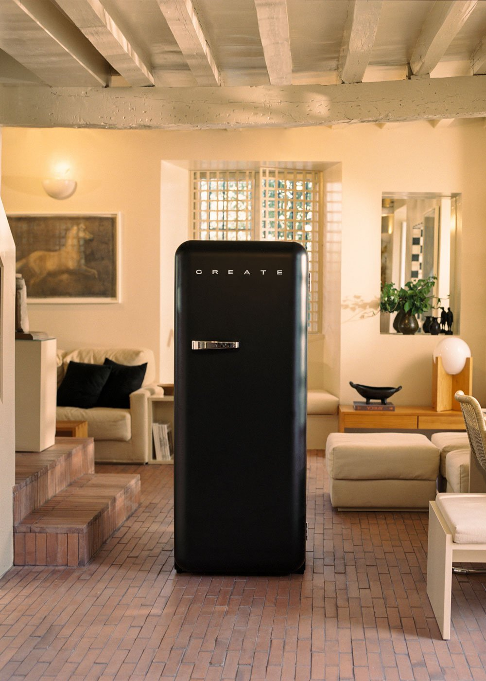 Un refrigerador negro está en una habitación. La palabra CREATE está en la puerta. Paredes beige, vigas de madera y un suelo de ladrillo son visibles.