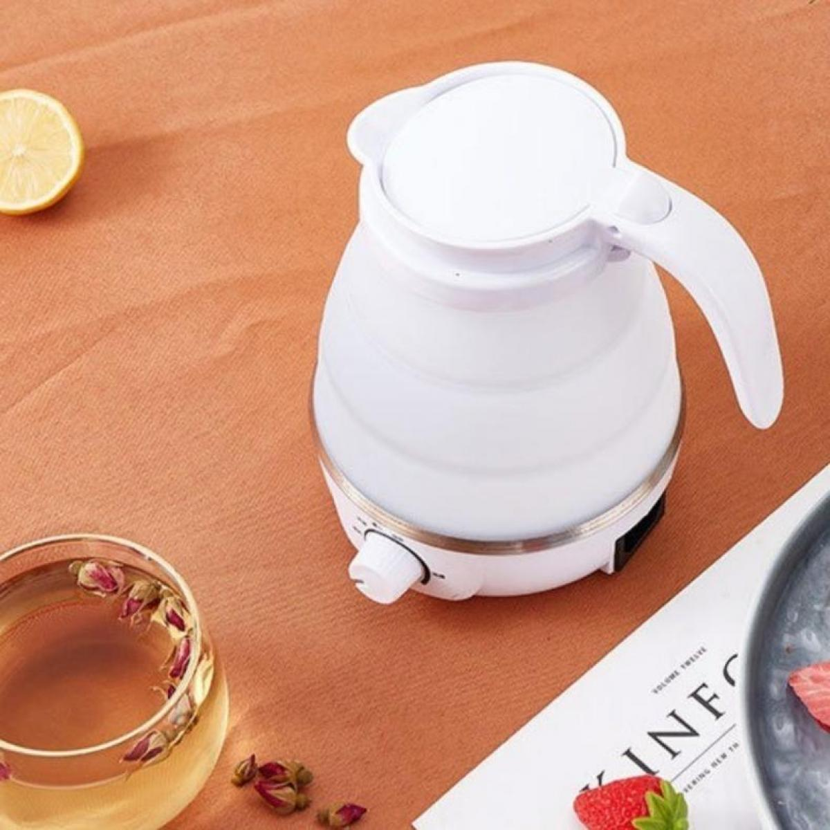 Weißer Wasserkocher, Zitronenhälfte, Tee im Glas mit Rosenknospen, Zeitschrift und Erdbeere auf orangefarbener Oberfläche.