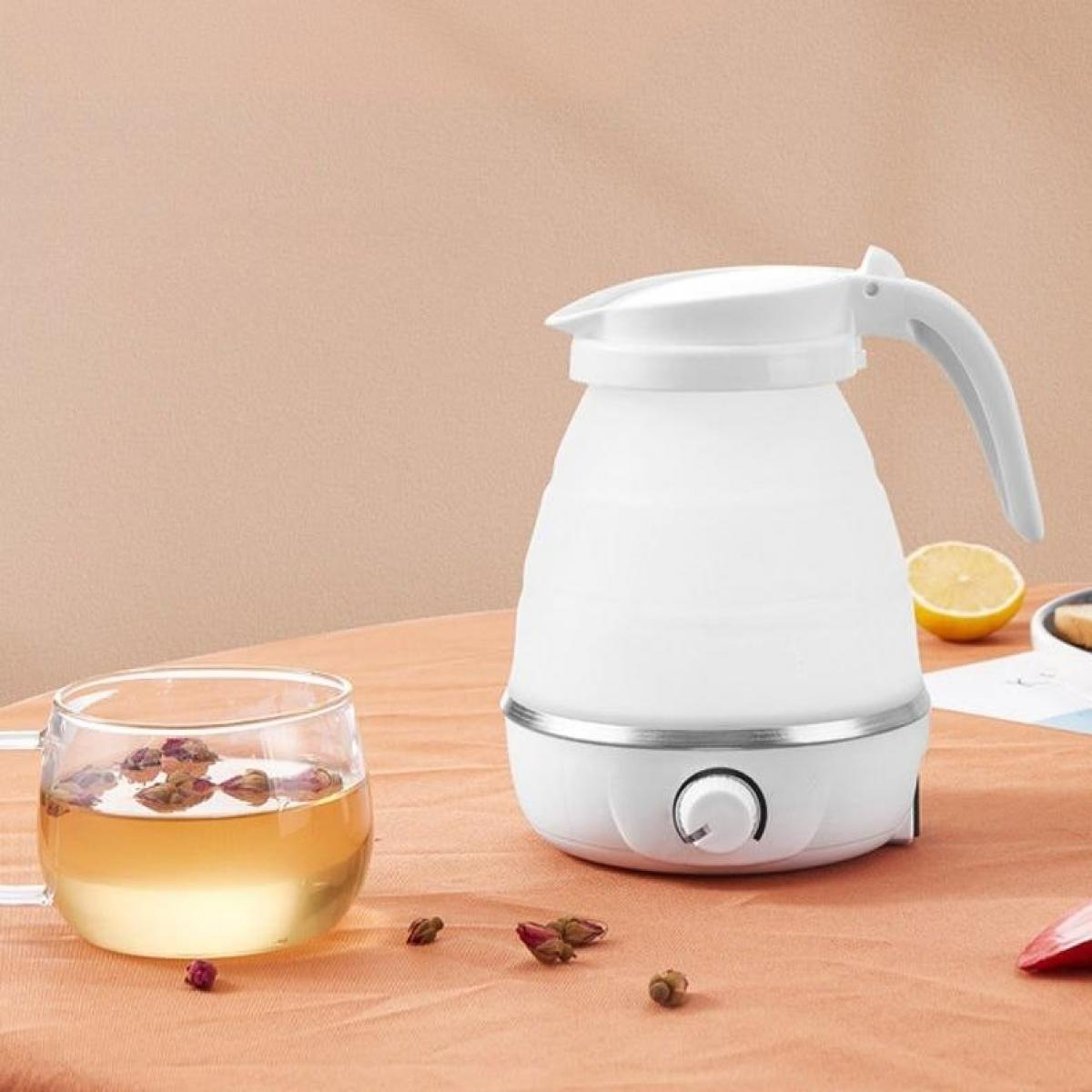 Ein weißer Wasserkocher und ein Glas Tee mit Rosenknospen. Eine Zitronenscheibe liegt neben dem Wasserkocher auf dem Tisch.